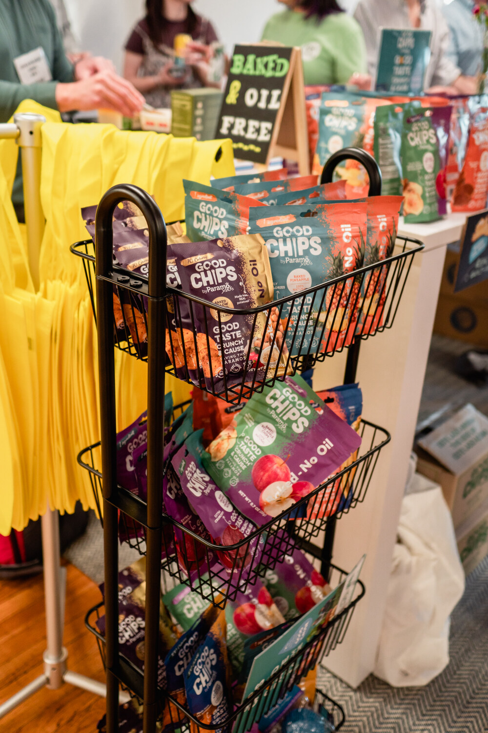 A wire rack stacked with colorful Good Chips bags beside a sign reading Baked and Oil Free.
