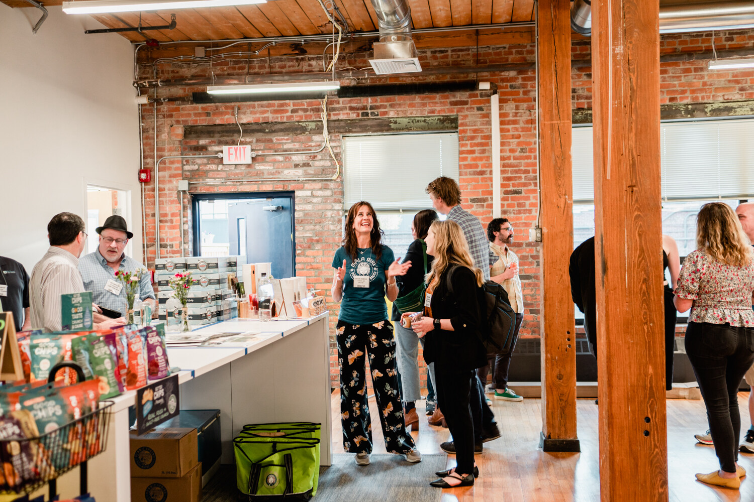 Wide view of guests standing around a long white table with product displays in a brick-walled loft office.