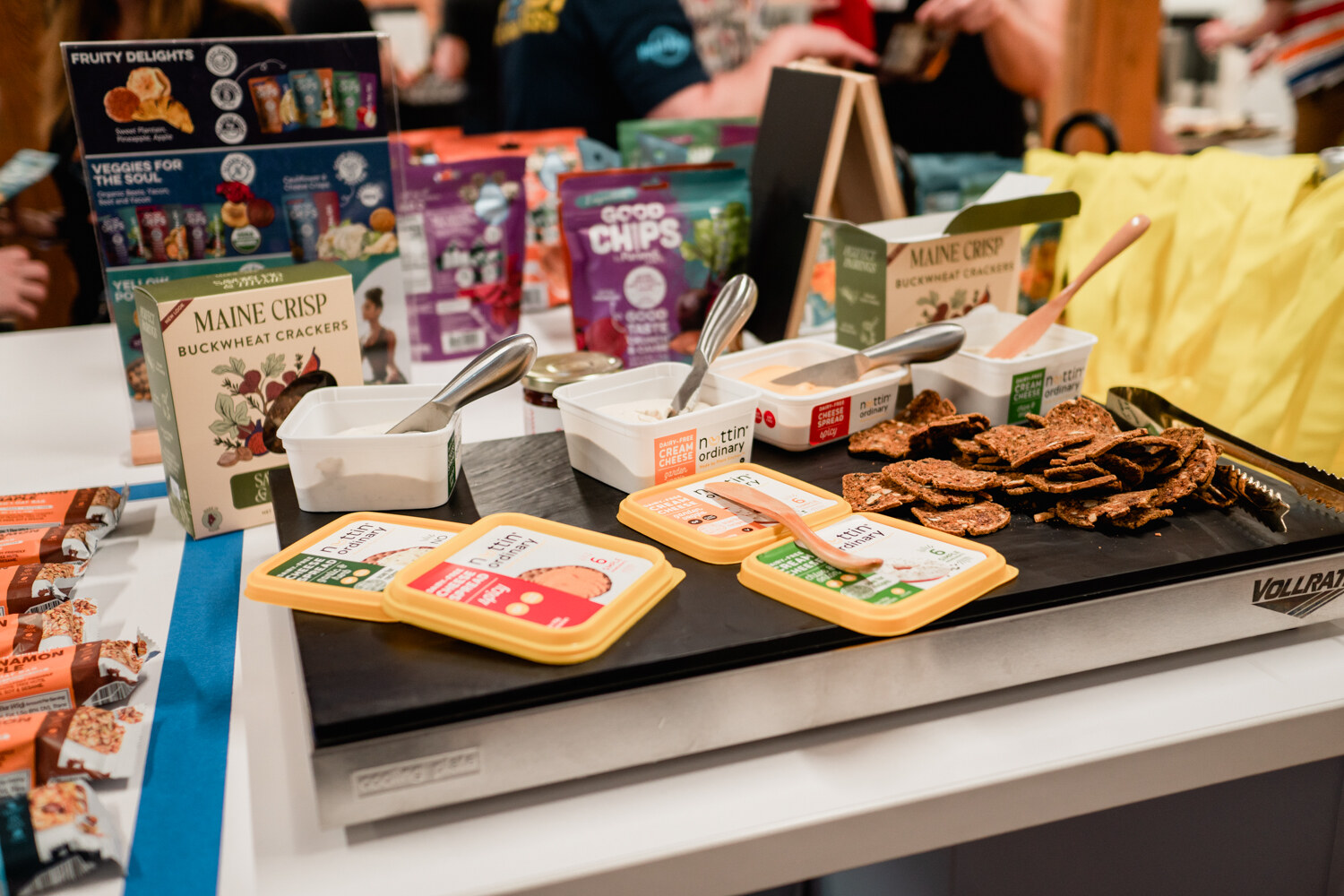 A black tray holding Maine Crisp buckwheat crackers and slices of cheese beside a Good Chips display.