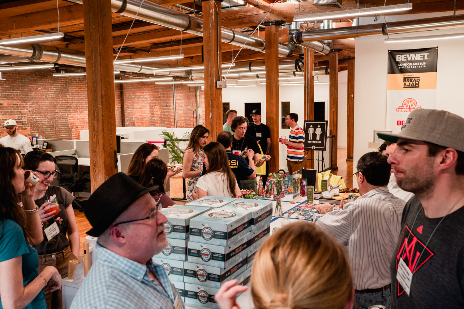 Guests stand around a long table of boxed products near a BevNET banner hanging on a brick wall.