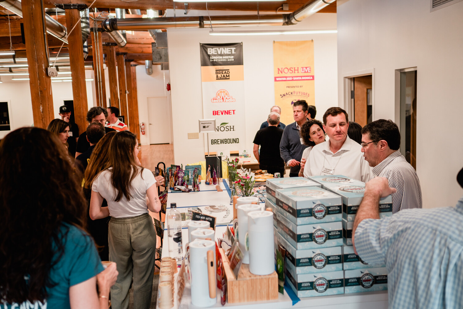 Looking down the office to banners for BevNET, NOSH and Brewbound with guests clustered around tables of products.