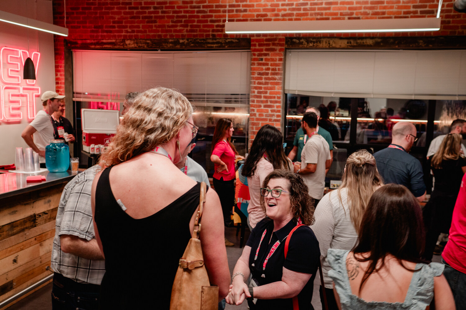Crowded view of guests talking in the office with the pink BEVNET neon sign in the background.