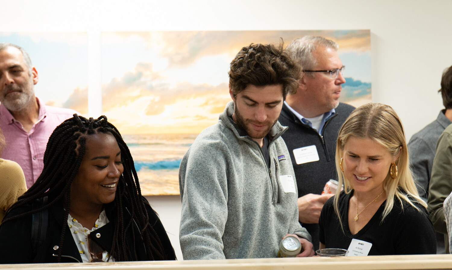 A group of guests with name tags stand at a wooden counter in front of a beach pier mural