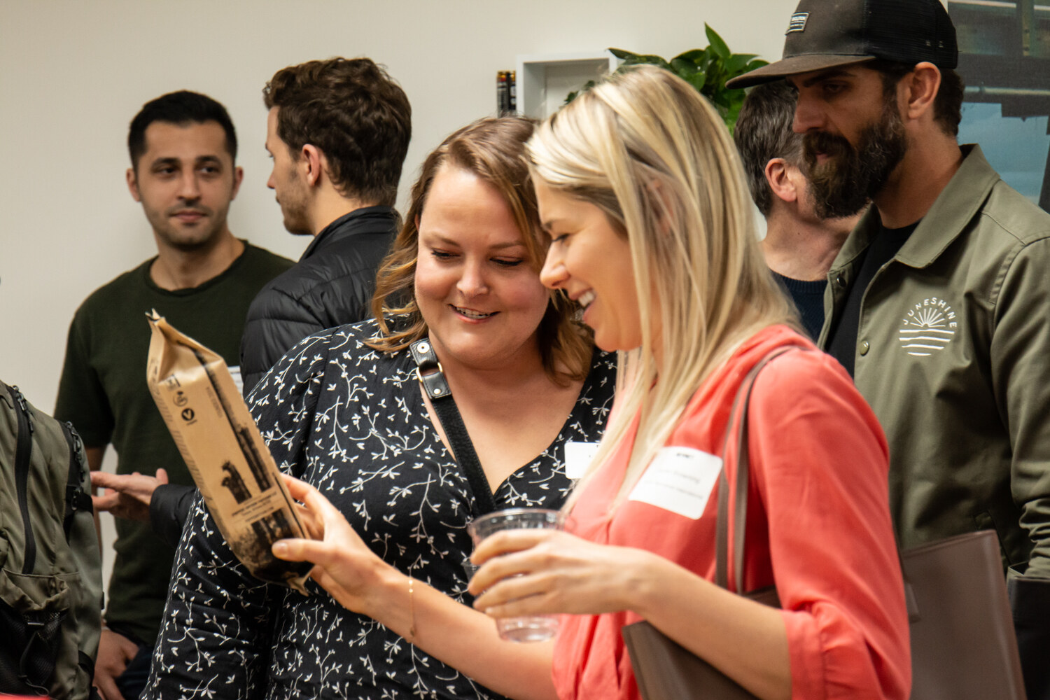 Two women with name tags look down at a brown coffee bag while others stand behind them
