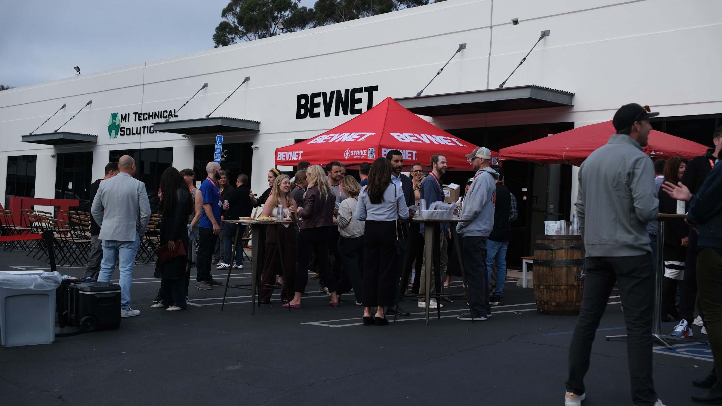A wide view of guests gathered in a parking lot in front of a building with a BEVNET sign and red tents.