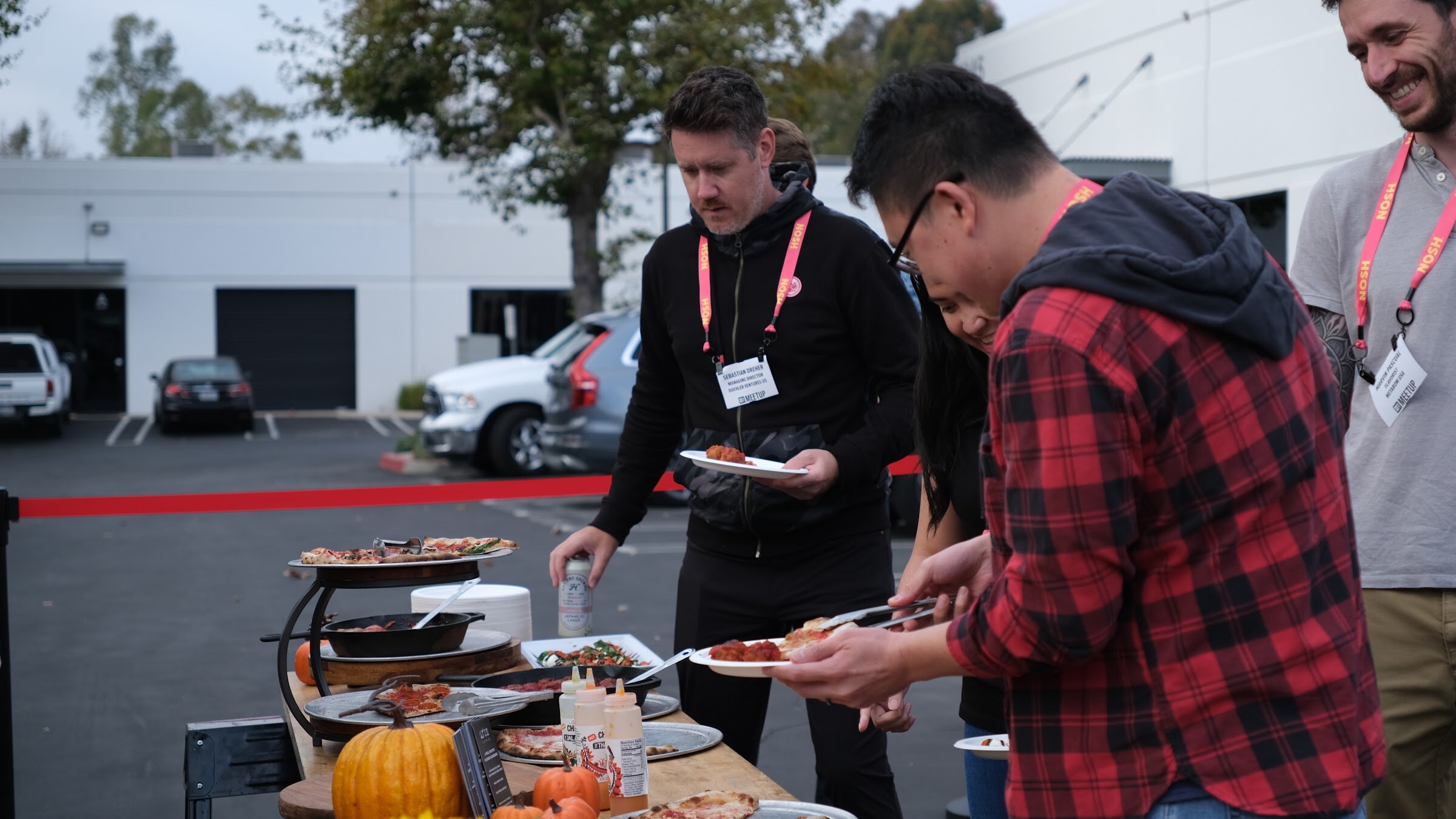 Guests with plates serve themselves from a buffet table with pizza, a pumpkin and sunflowers.