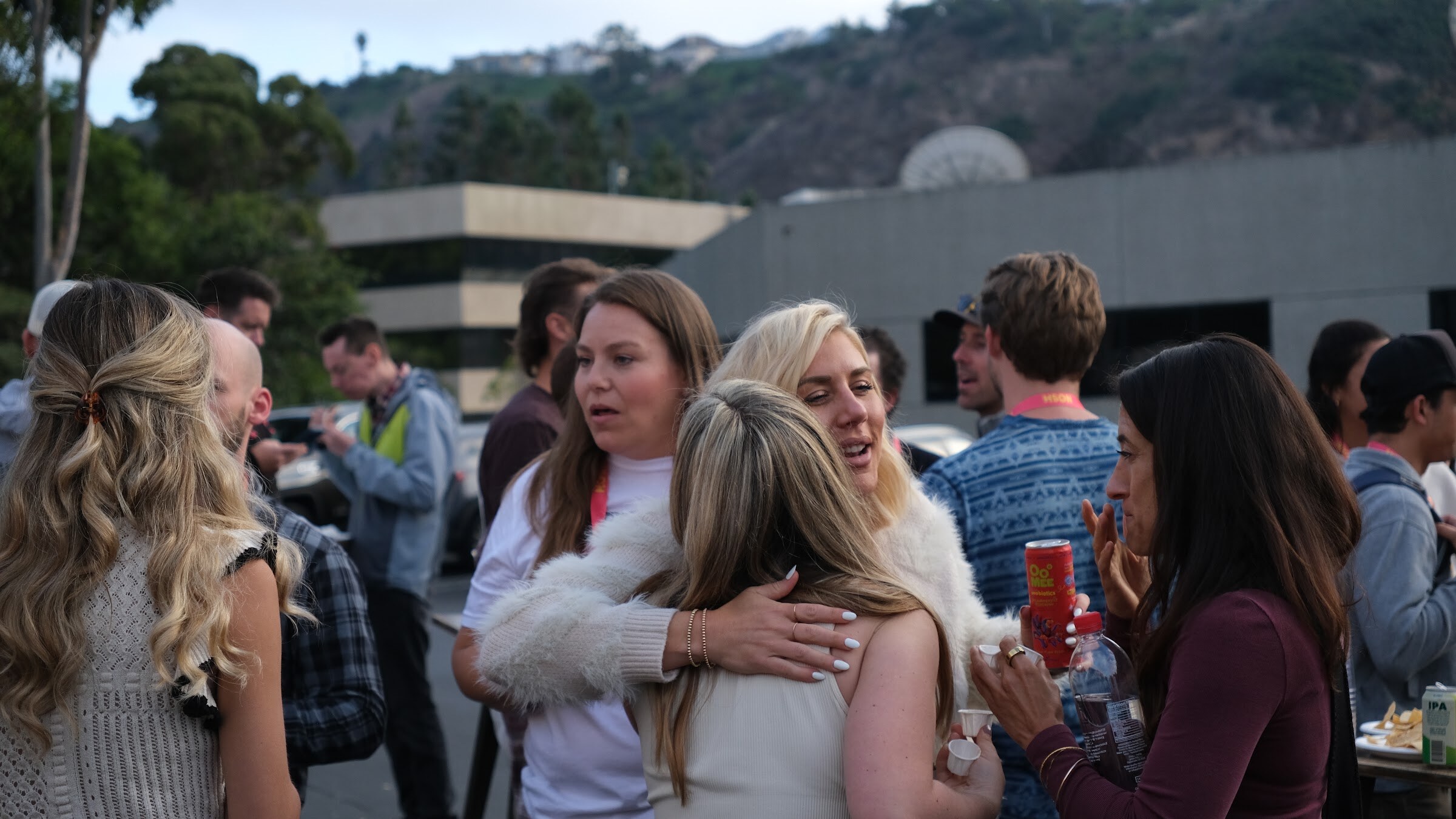 Two women hug in a crowd of attendees standing in a parking lot.
