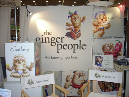 A booth display for the ginger people with illustrated ginger characters on panels, a sign reading We know ginger best, and director's chairs printed with A good root.