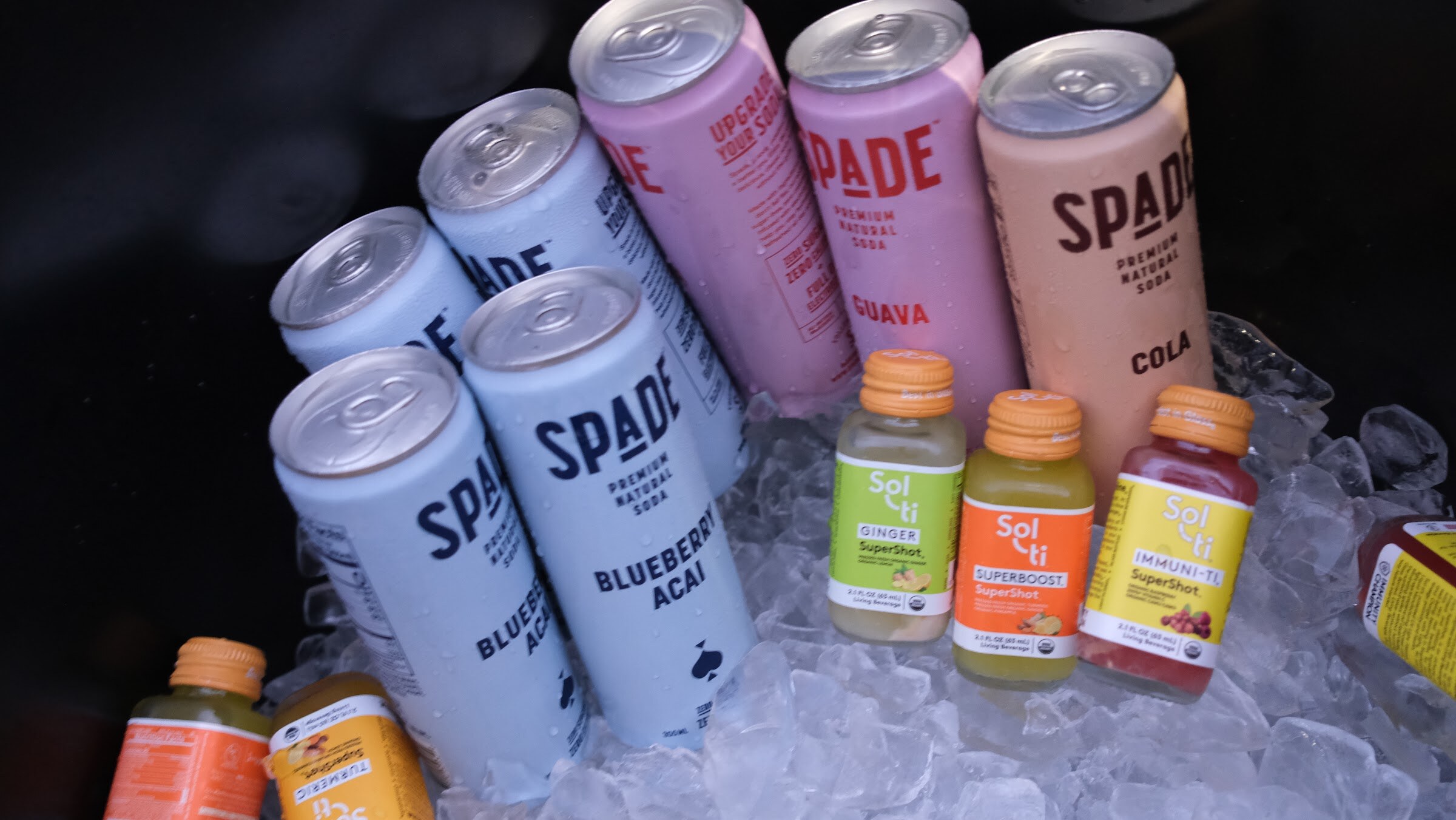 Spade cans in blueberry acai, guava and cola flavors beside small Sol-ti bottles in a bed of ice.