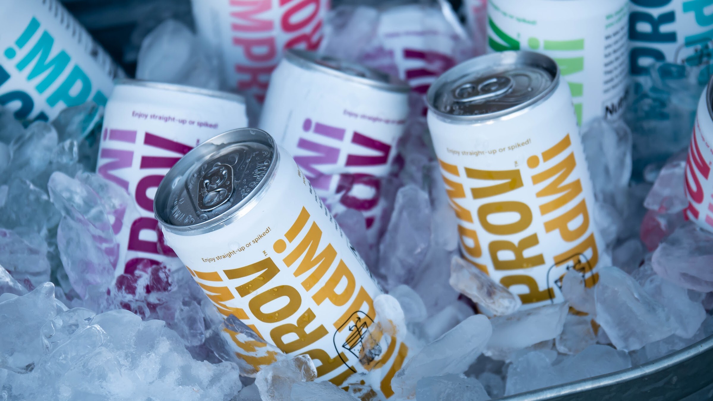 Cans of Improv sparkling drinks in yellow and purple chilling in a bucket of ice.