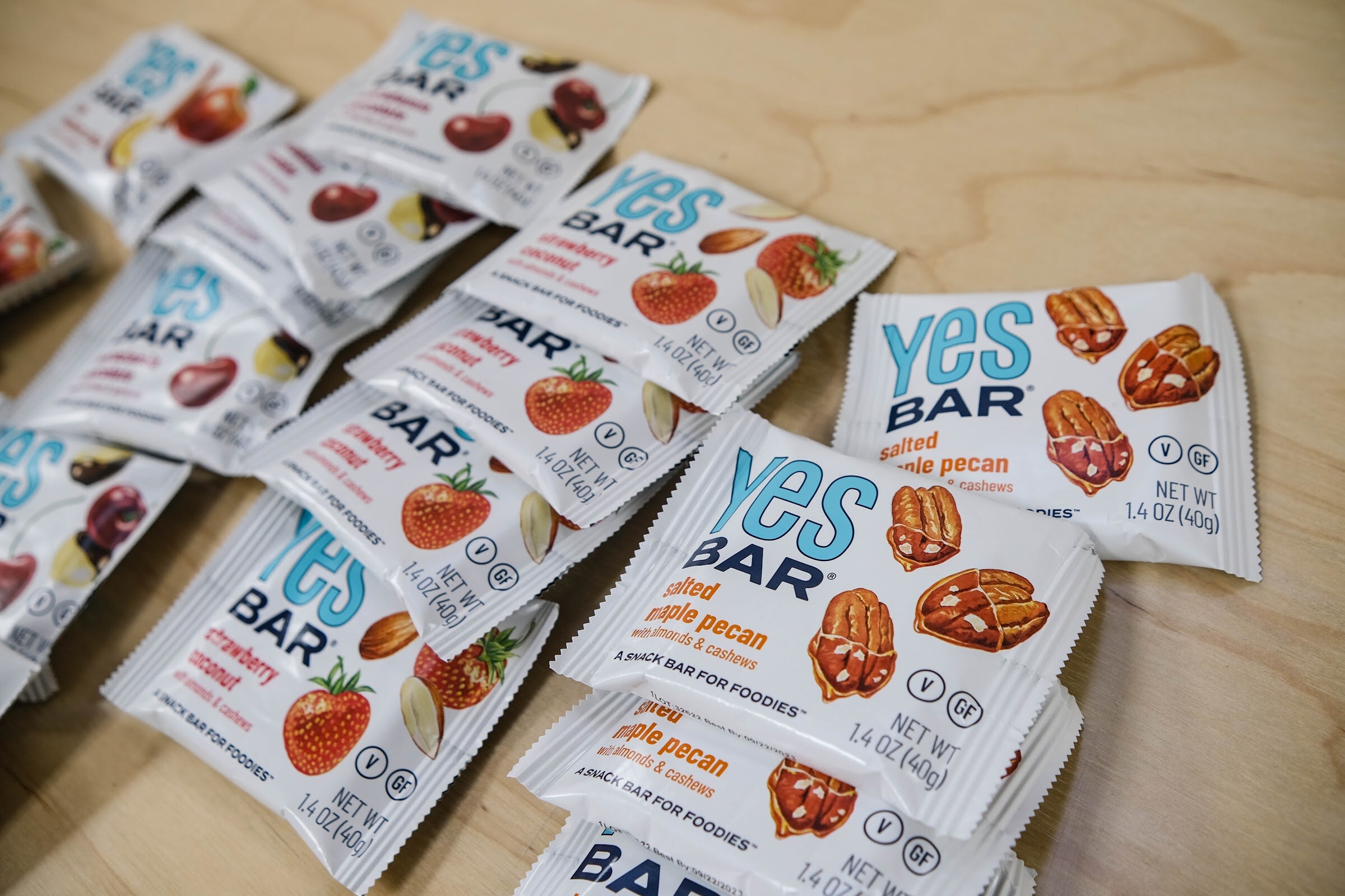 Close-up of Yes Bar packages in strawberry and salted pecan flavors on a light wood table.