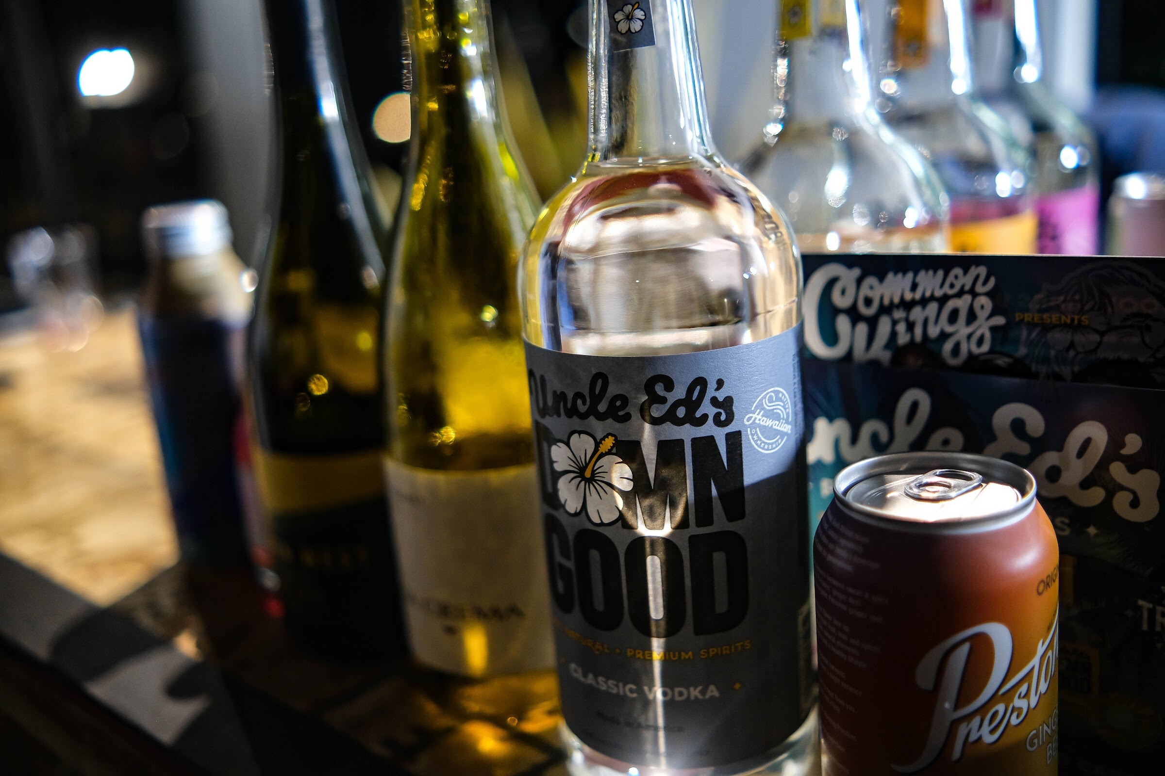 Close-up of a bottle labeled Uncle Ed's Down Good vodka next to wine bottles and a can of Preston's soda.