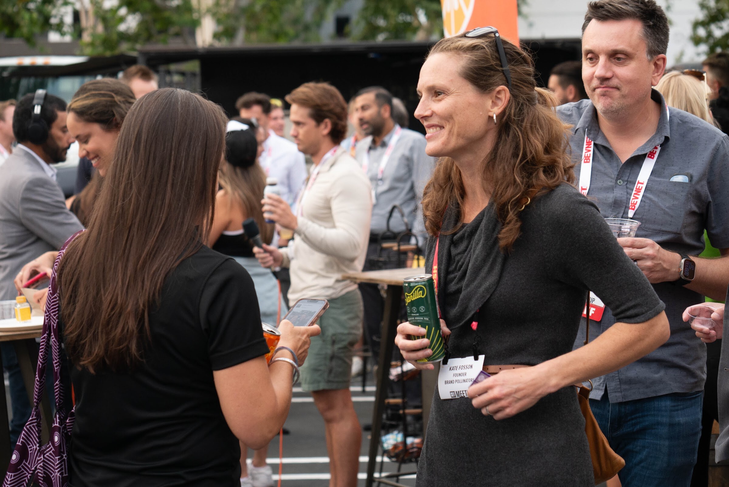 A smiling woman in a gray top talks with a man while other guests mingle around tall tables.