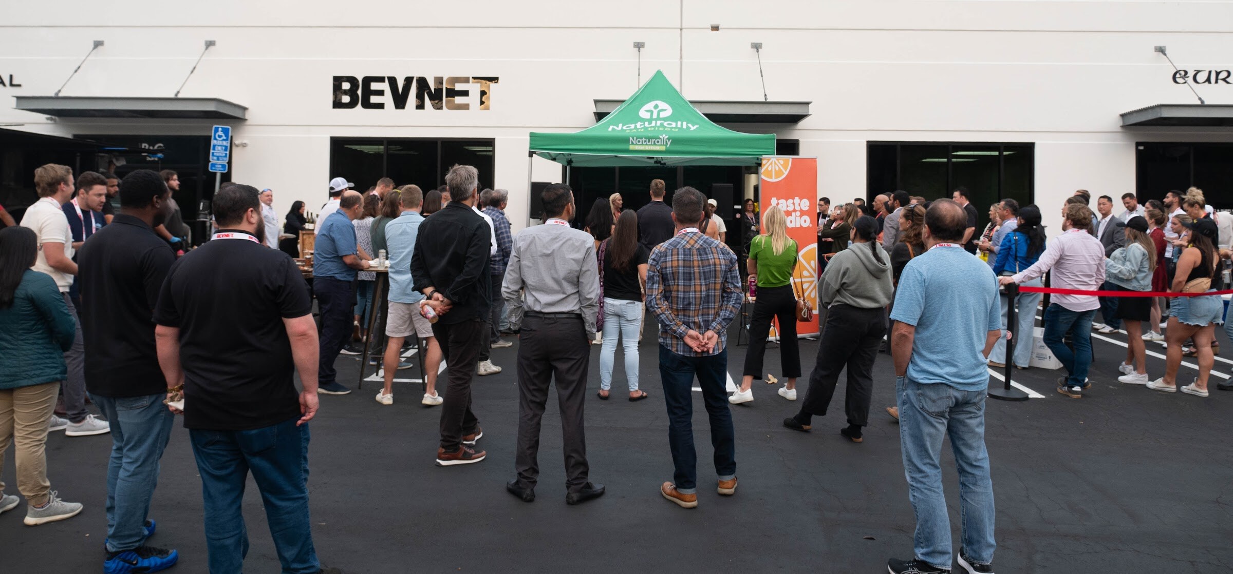 Wide view of guests standing in a lot in front of the BevNET building and green tent.