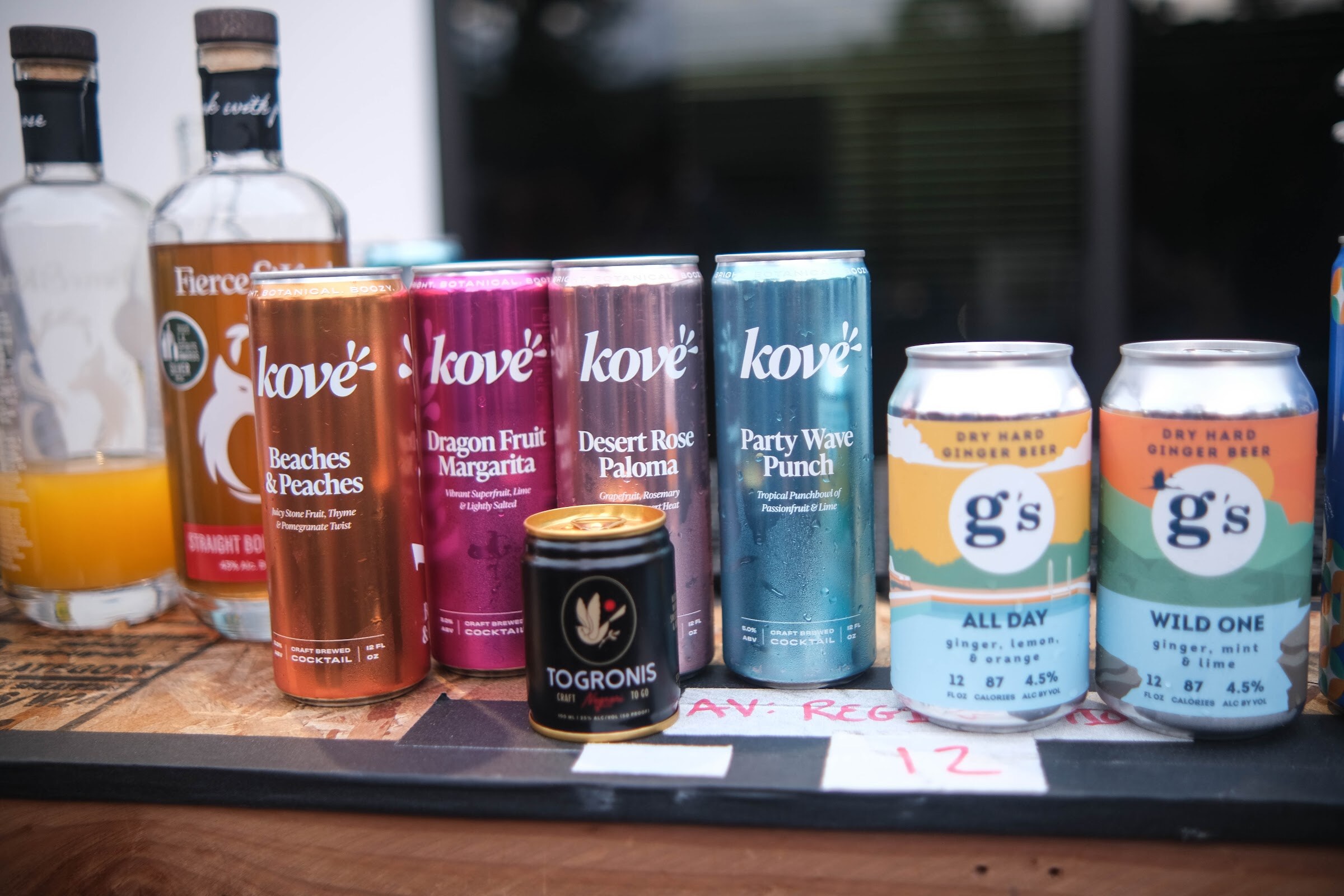 A row of canned drinks including Kove cocktails and g's dry hard ginger beer on a wooden counter.