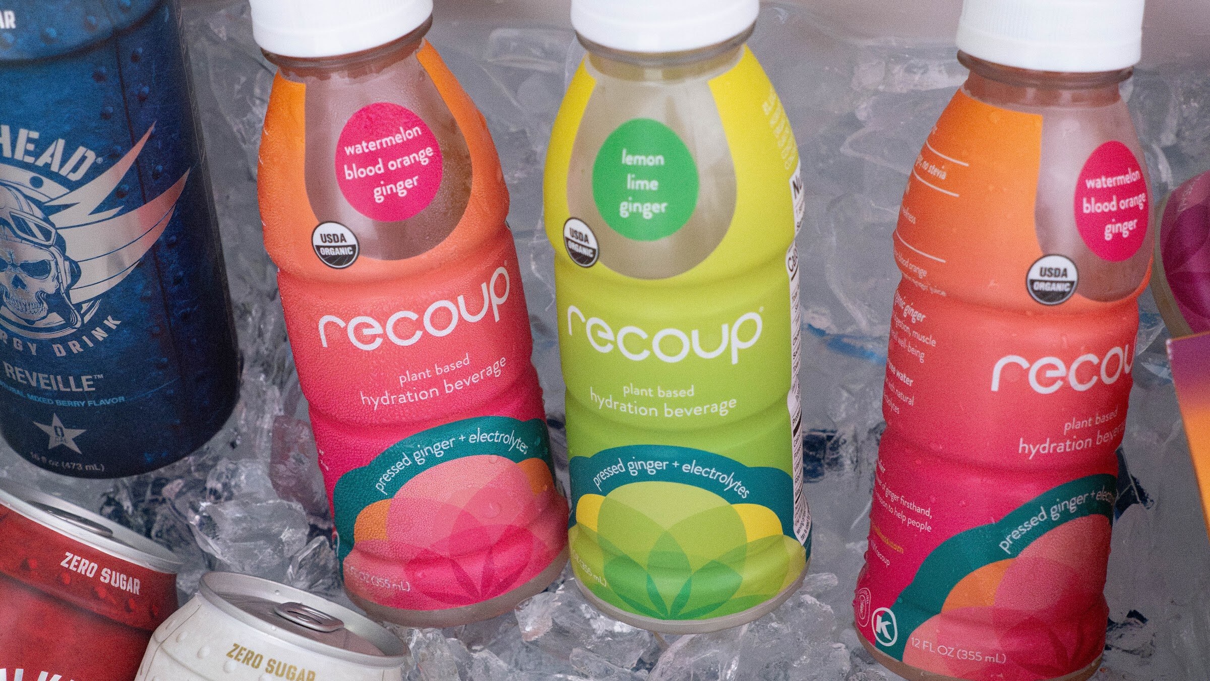 Plant-based Recoup hydration beverages in several flavors sitting in ice next to Bulkhead cans.