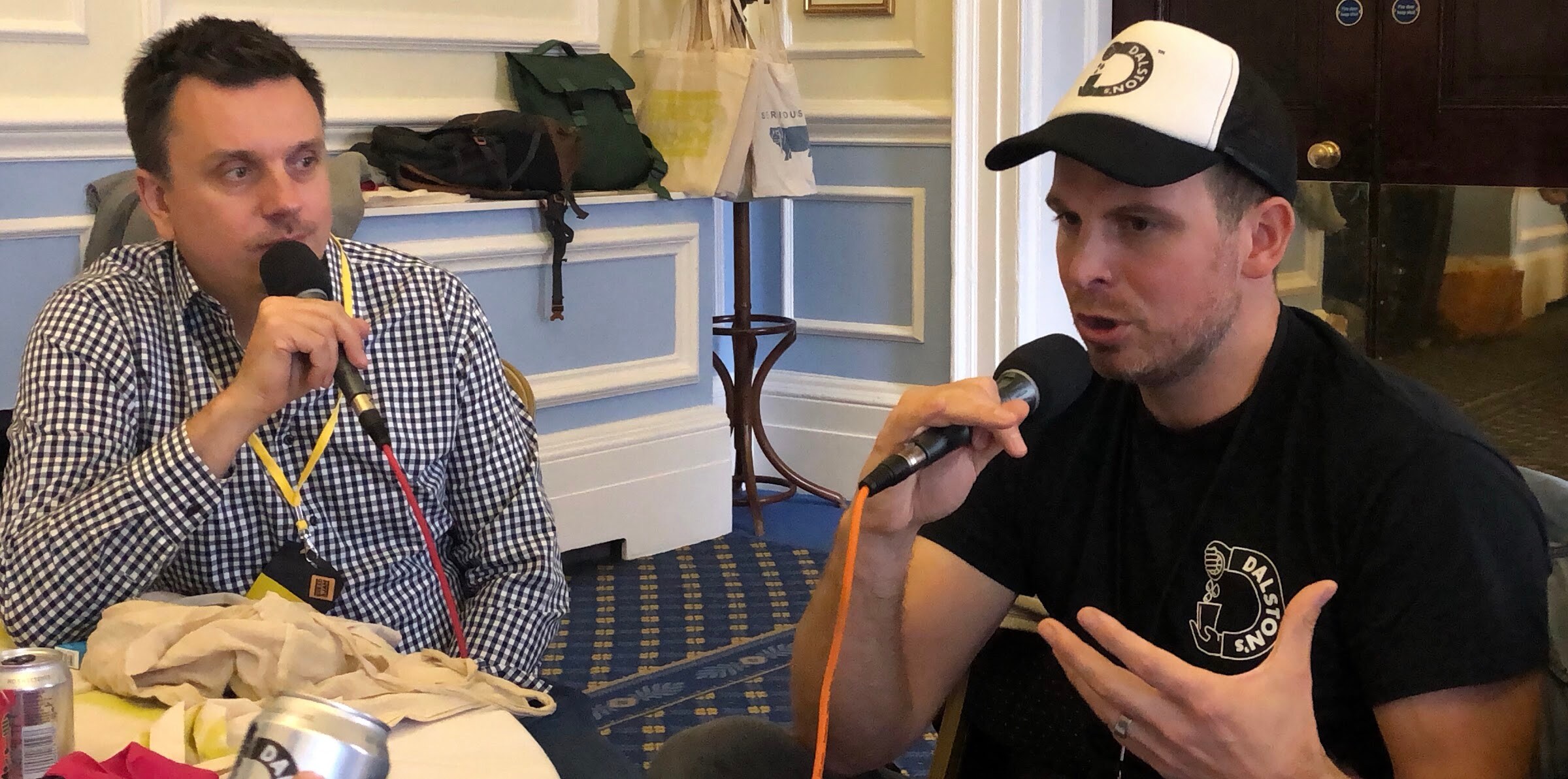 A man in a checked shirt and a man in a black Dalston's cap speaking into microphones across a table.