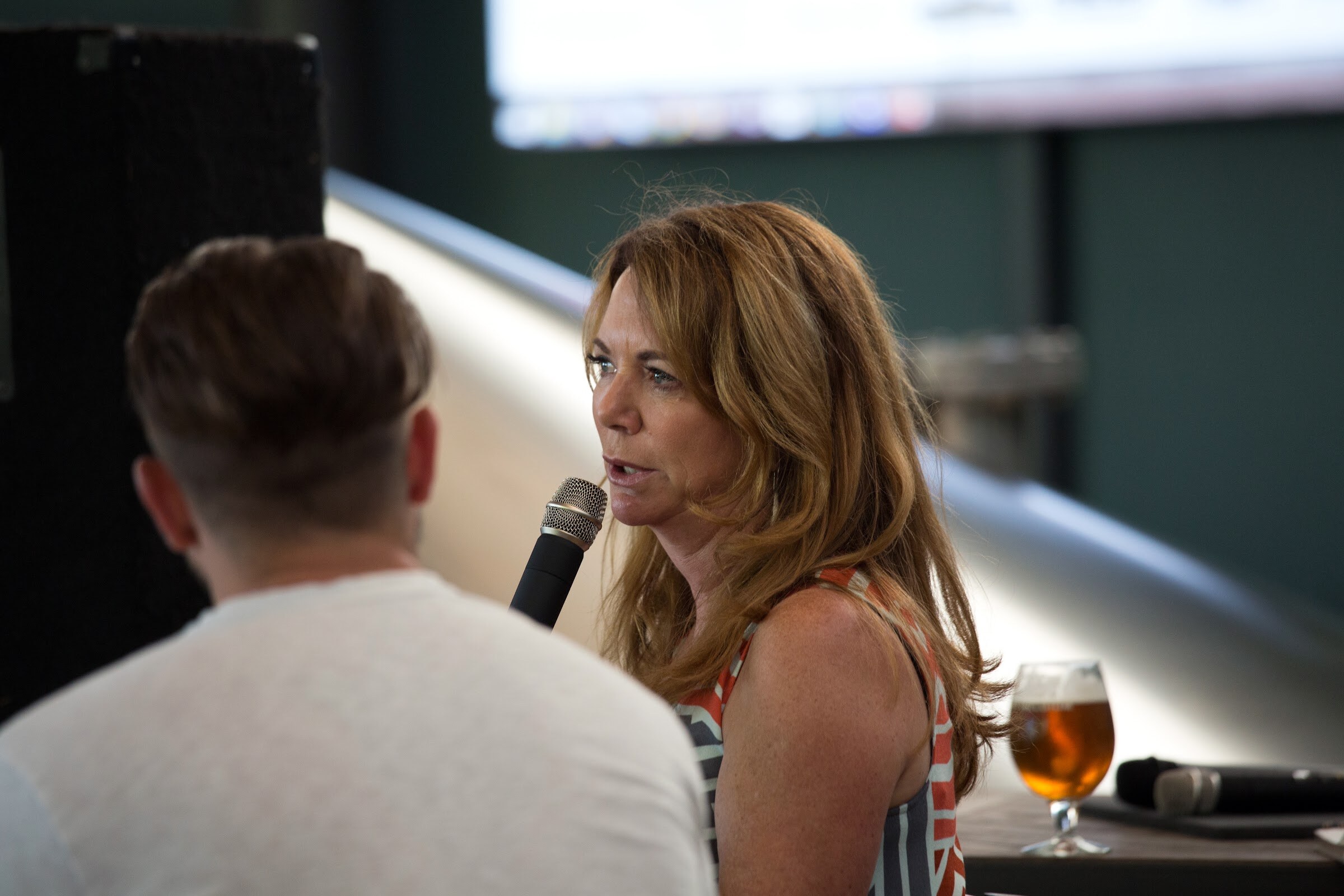 A woman holds a microphone near her mouth while facing a seated man in a white shirt.