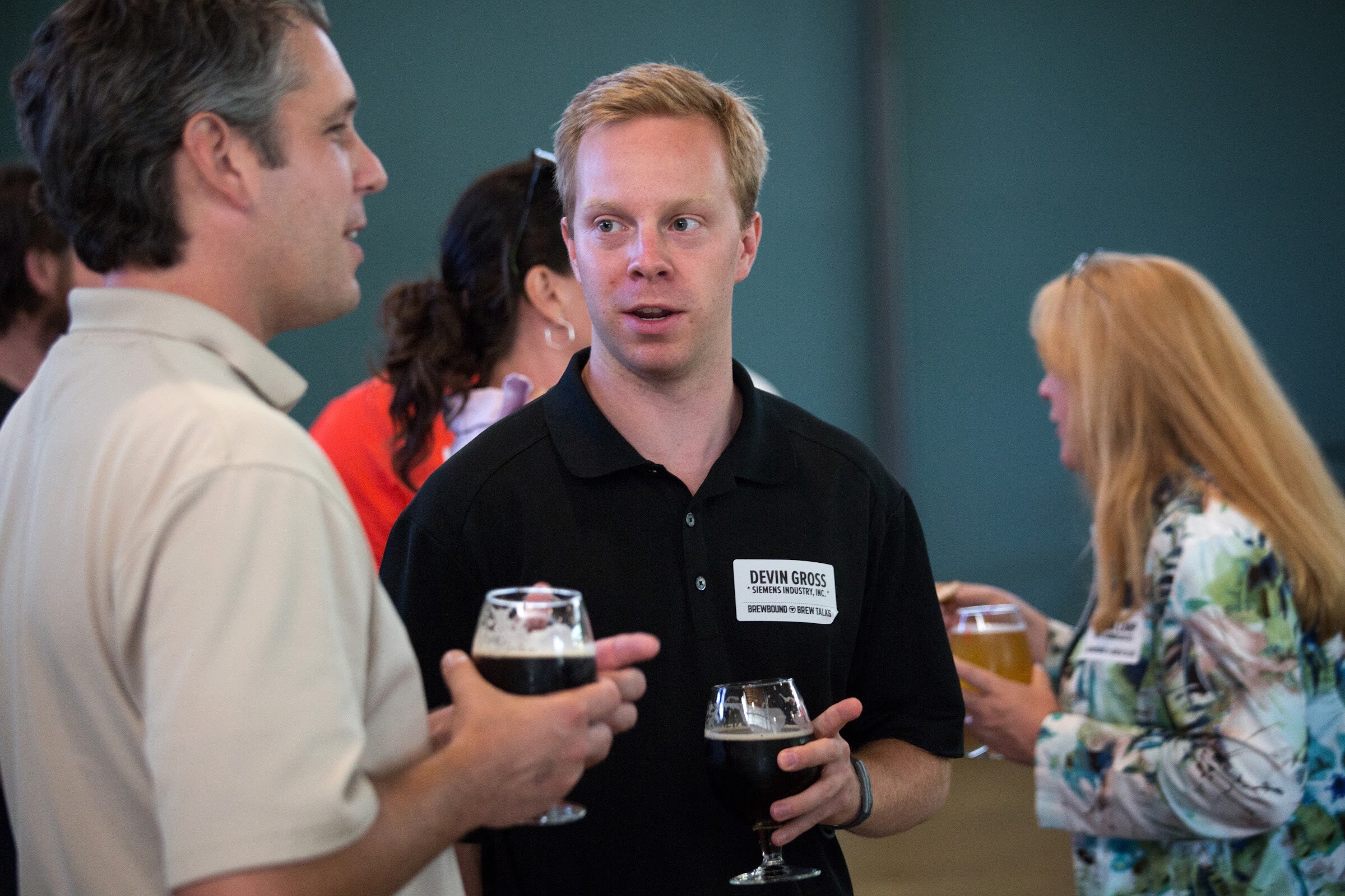 Men in beige and black polo shirts face one another with beer glasses in hand.