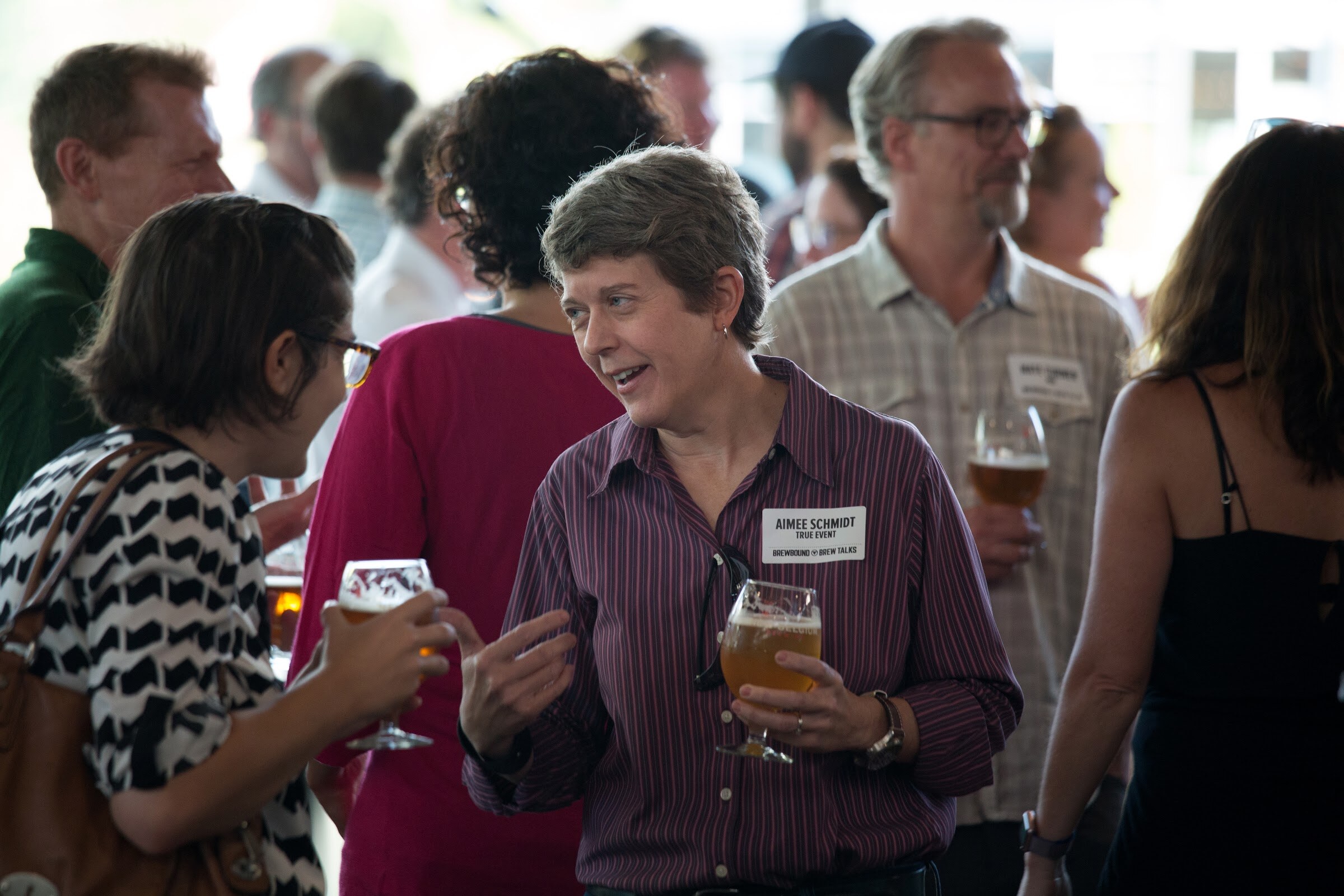 A person in a purple striped shirt gestures toward another guest in a crowded room.