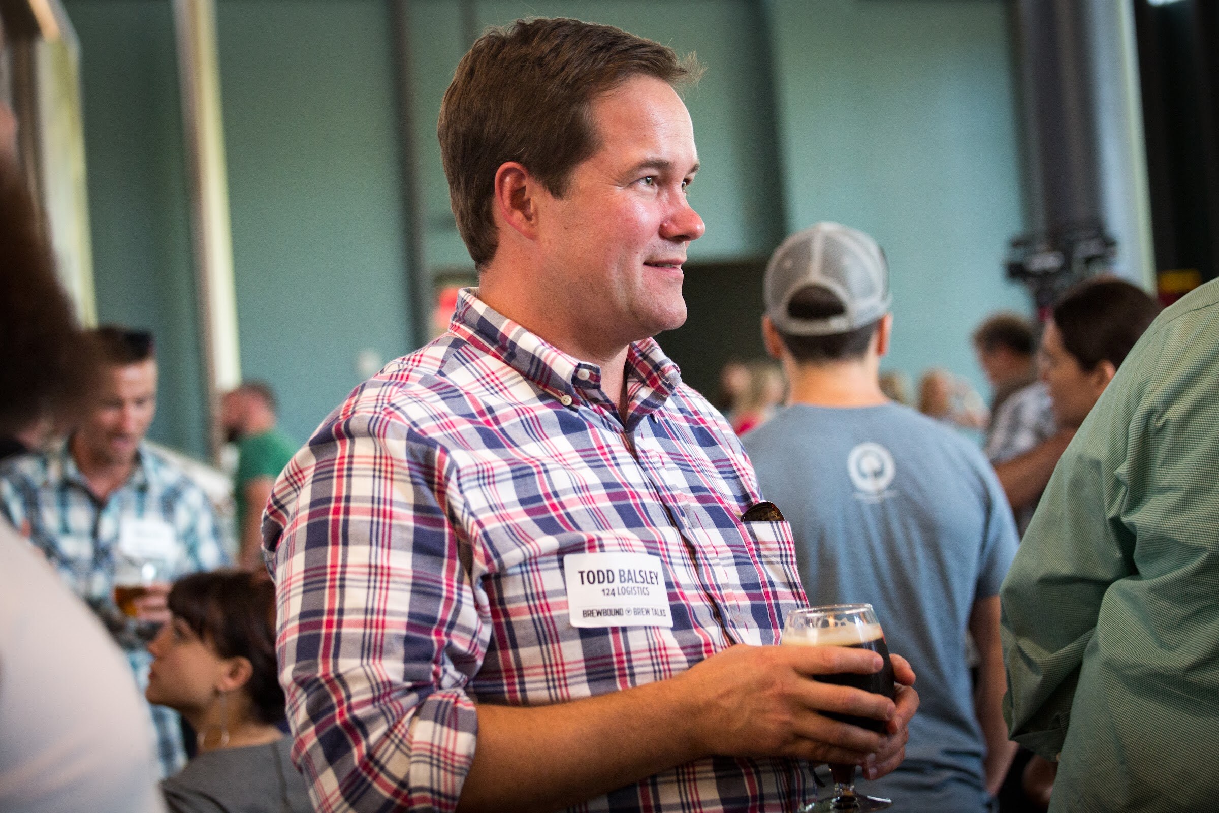 A man in a red, blue and white plaid shirt holds a beer glass and looks to the right.