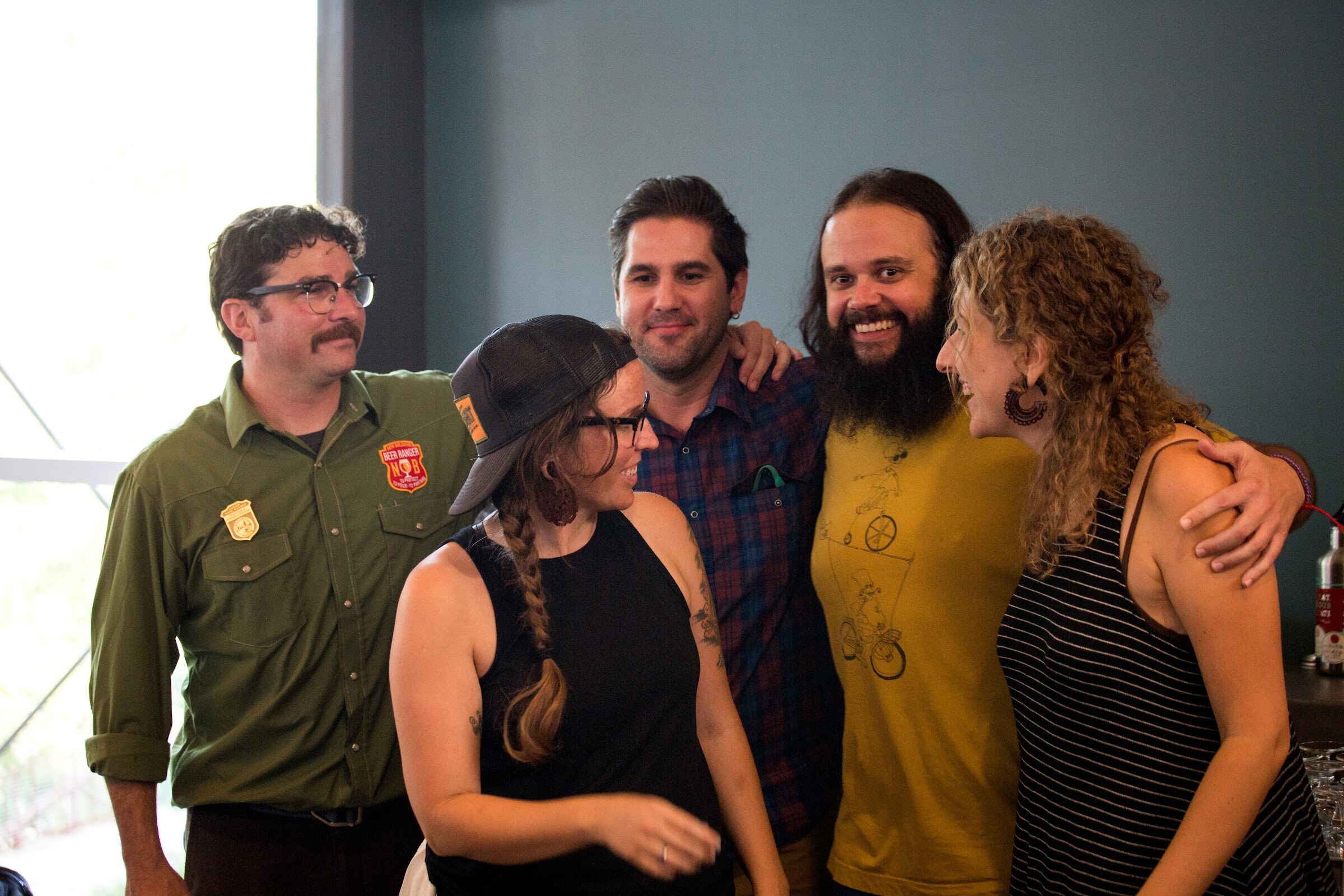 Five smiling people stand close together near a window and green wall.