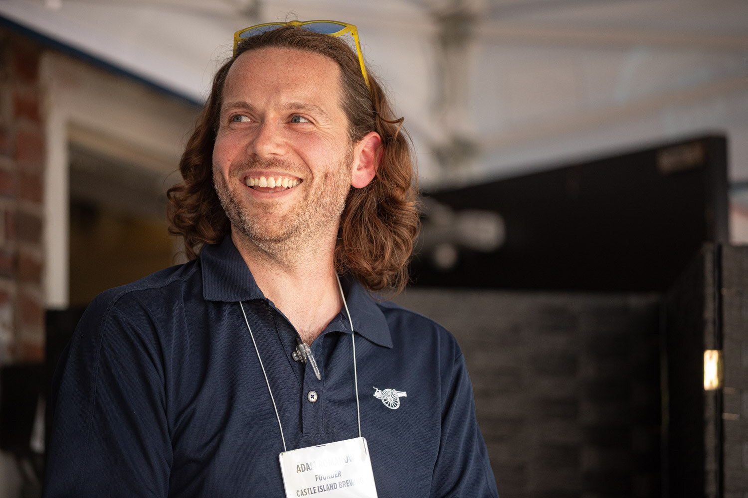 A man with shoulder-length hair and a navy polo laughs while looking off to the side.