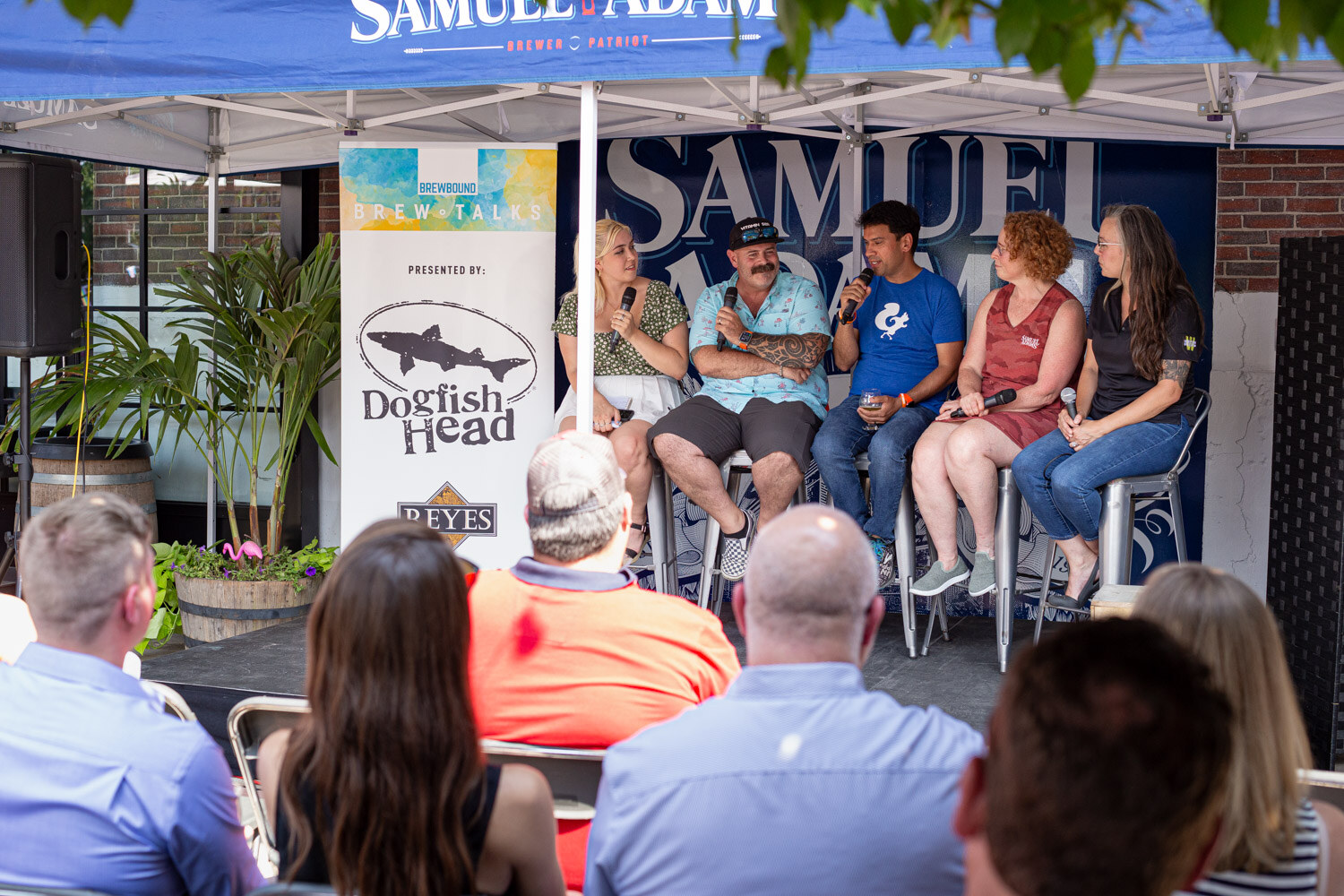 Wide view of five panelists on stools under a Samuel Adams tent with a Dogfish Head Brew Talks banner and audience seats in front.