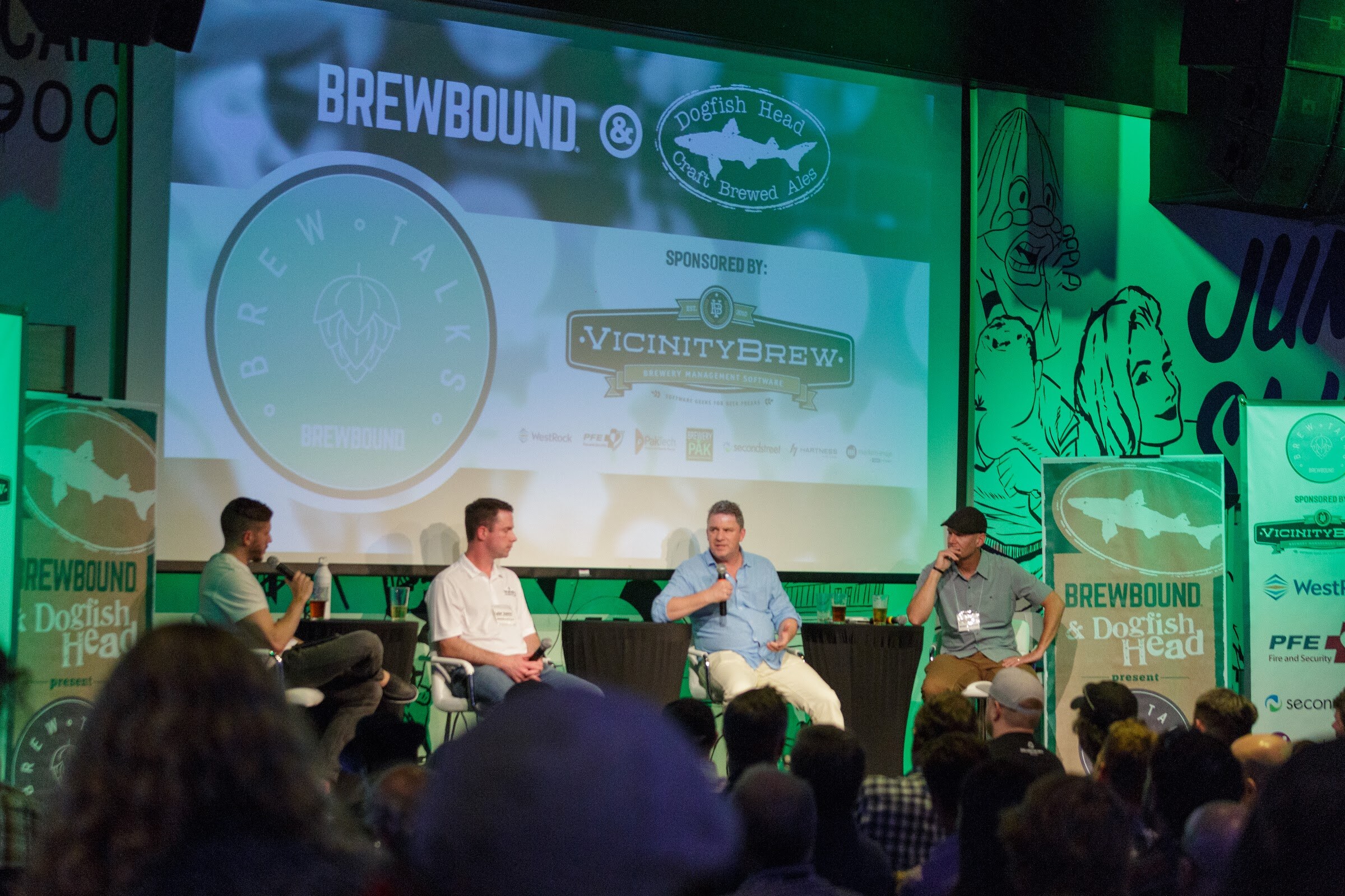 Four people sit on stage under a screen reading Brewbound and Dogfish Head, Brew Talks, sponsored by VicinityBrew, with audience heads in the foreground.
