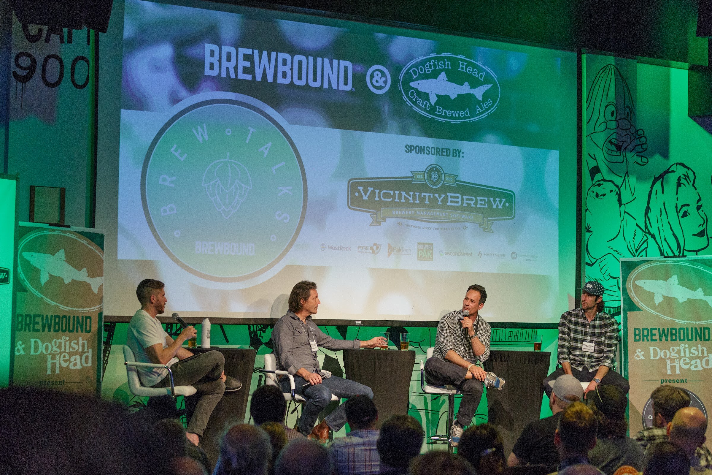 Four people on stage in front of a screen reading Brewbound and Dogfish Head Brew Talks, with silhouettes of the audience in the foreground.