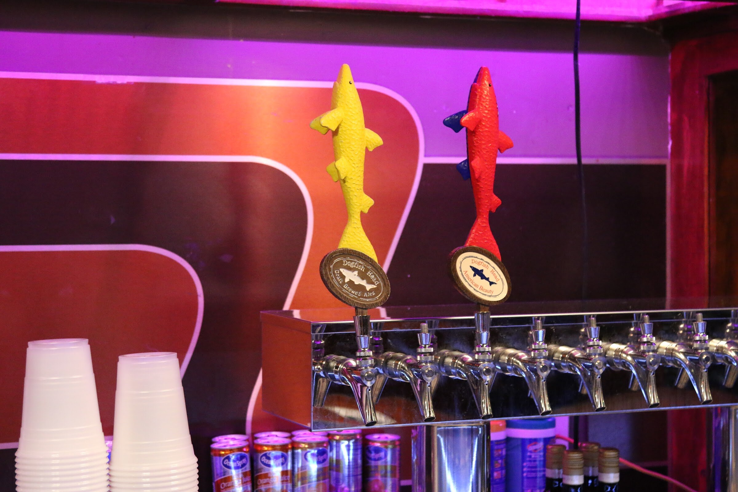 Two fish-shaped tap handles, one yellow and one red, above a row of chrome taps against a purple wall.