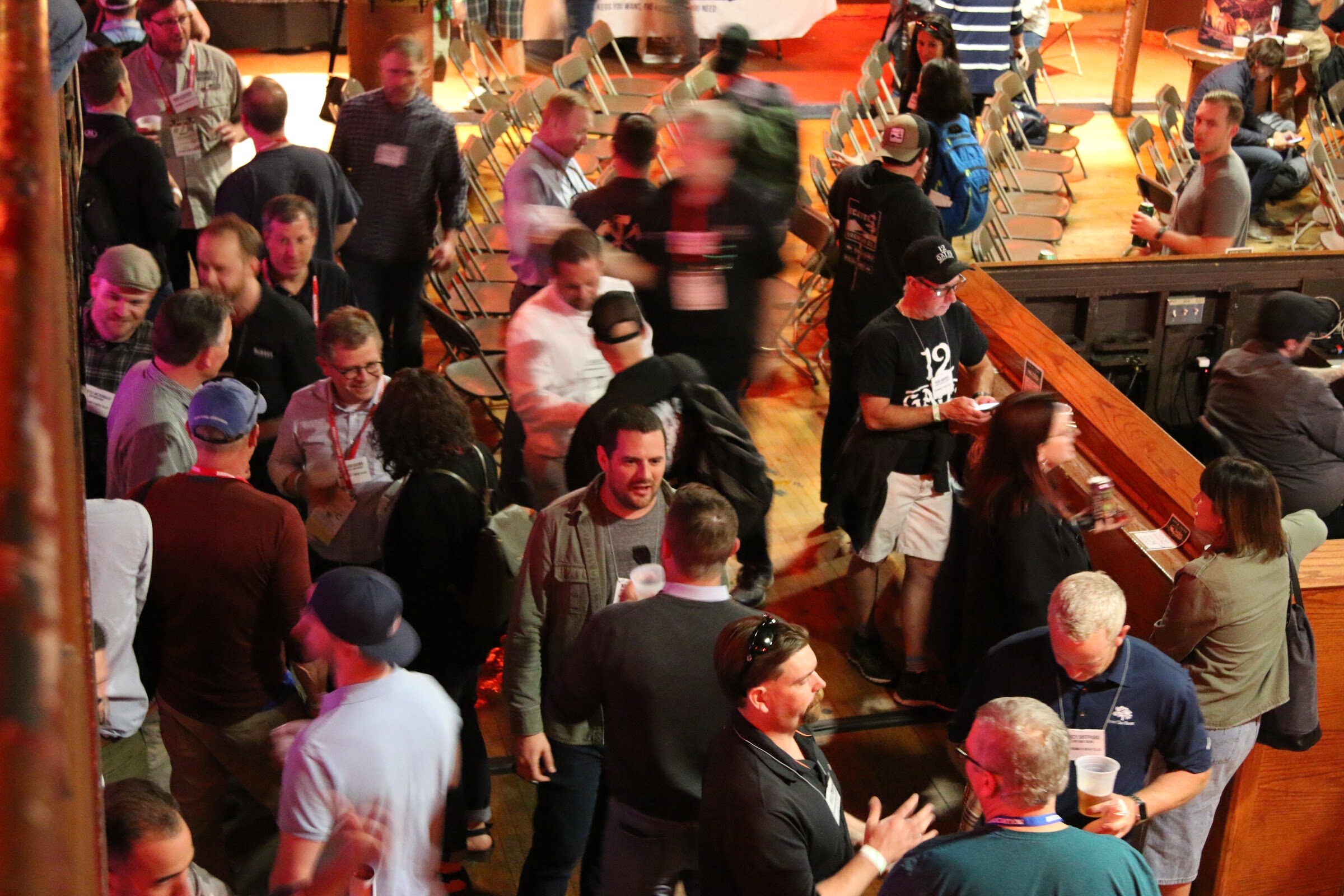 Overhead view of many attendees with name badges standing and talking between rows of folding chairs.