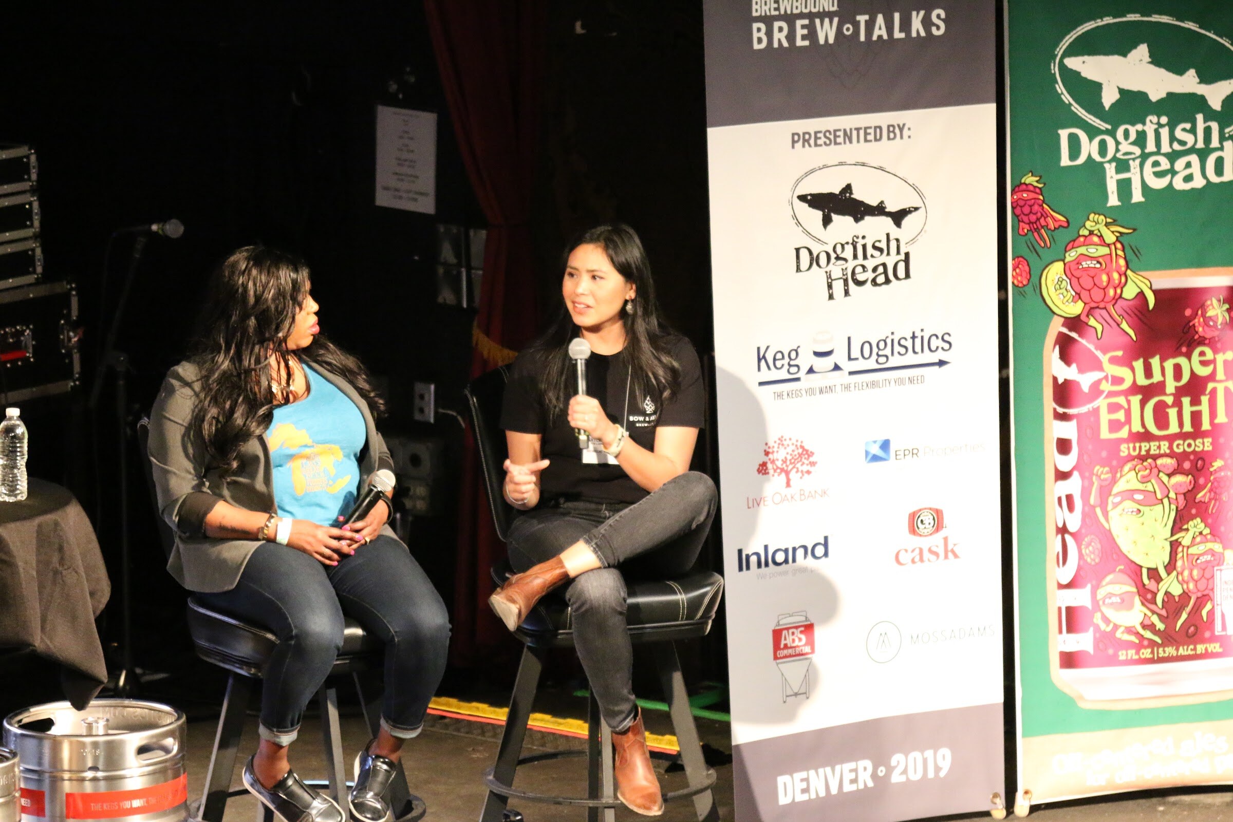 Two women seated on stools next to a Brewbound Brew Talks banner and a Dogfish Head SuperEIGHT banner reading Denver 2019.