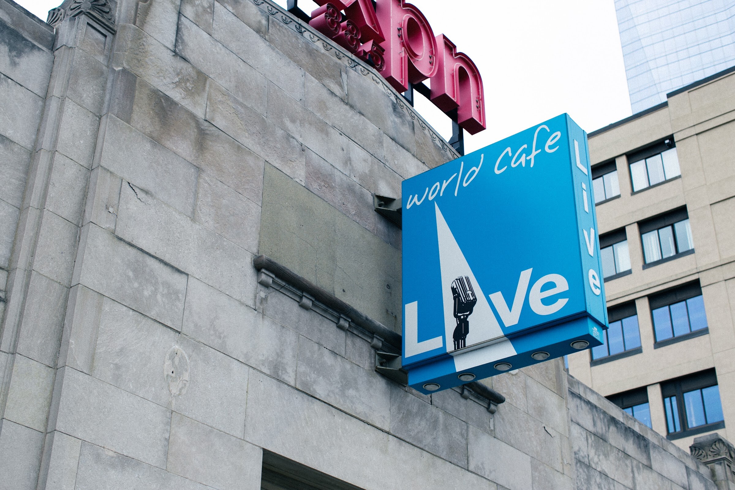 A blue World Cafe Live sign projects from a stone building beneath red WXPN letters.