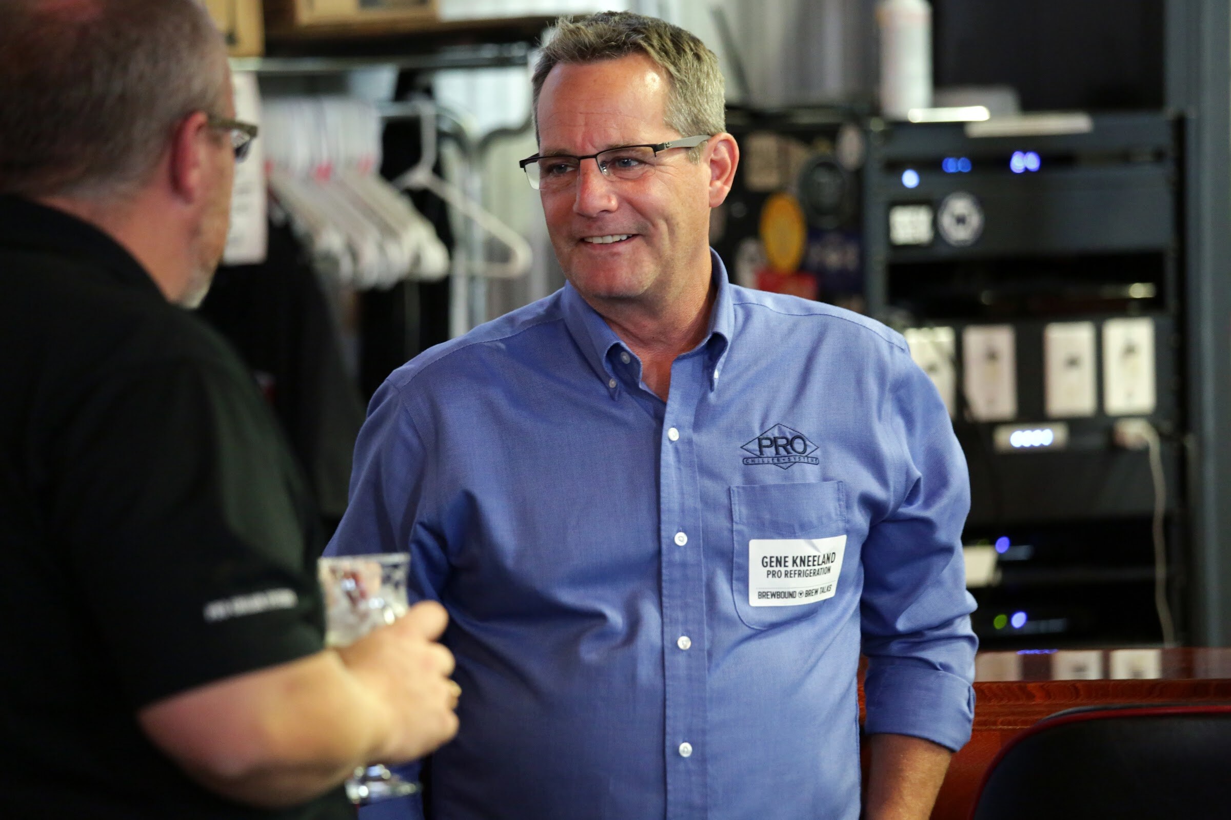 A man in a blue button-down shirt faces another guest holding a beer glass.
