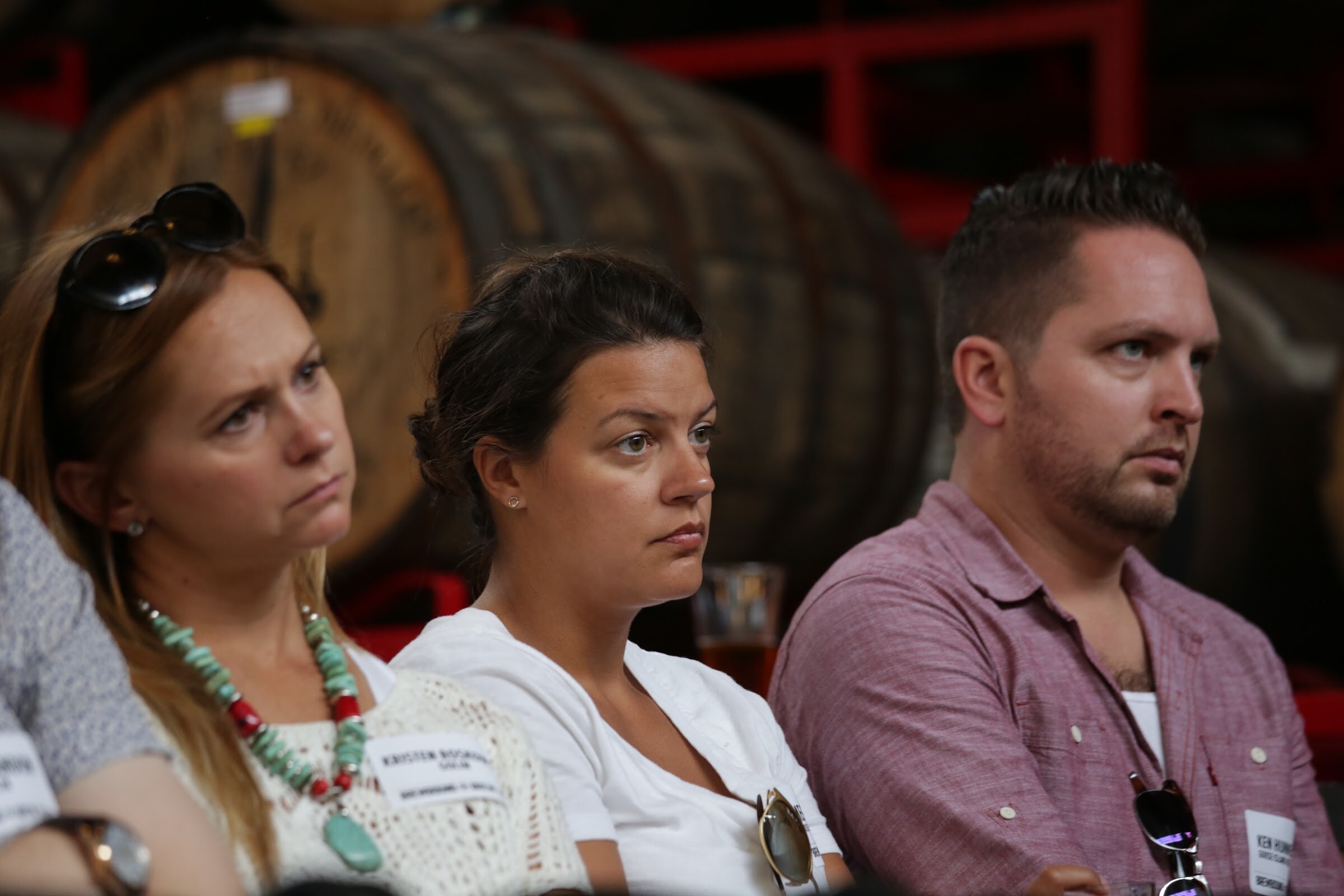 Two women and a man sit facing the stage with wooden barrels behind them.