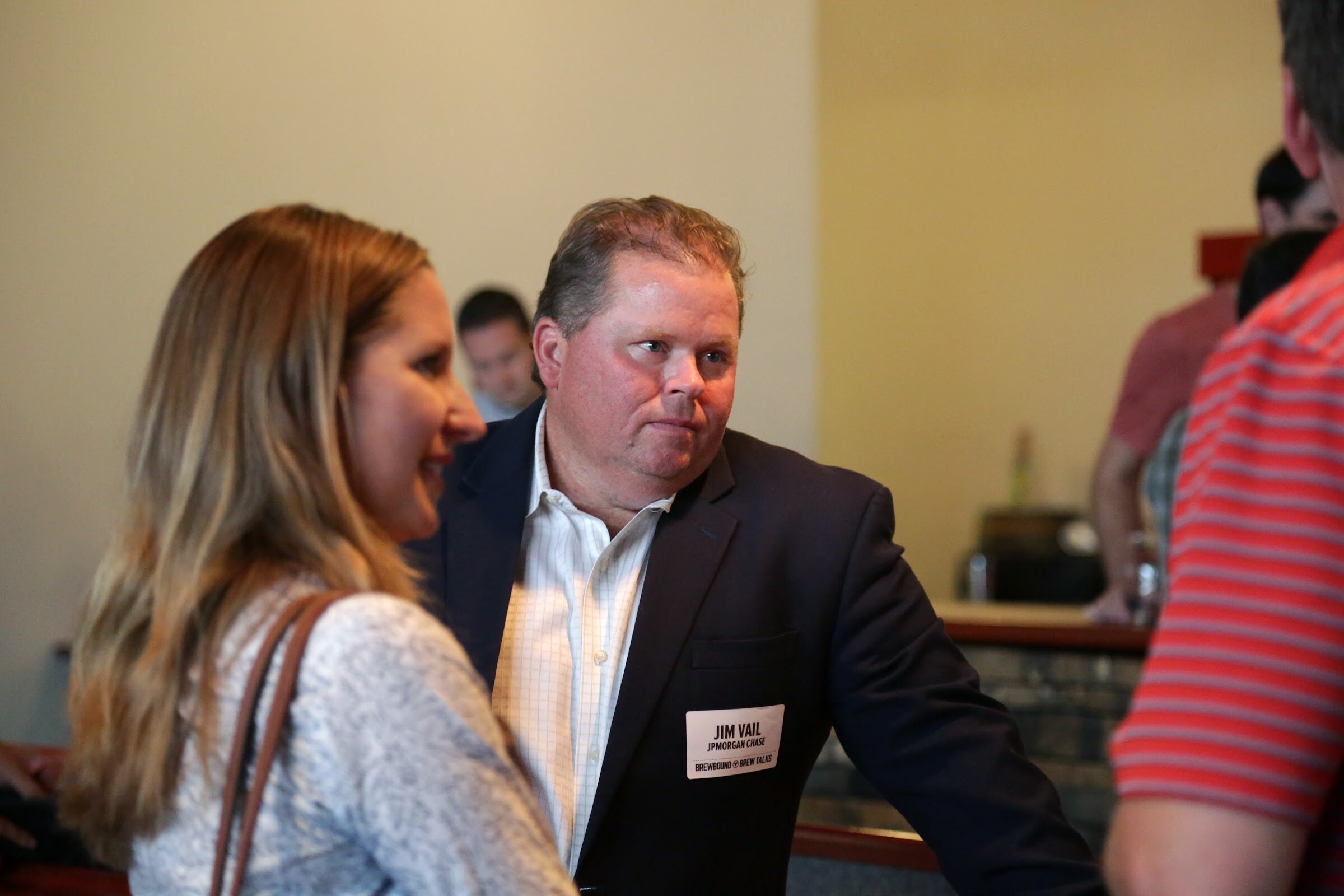 A man in a dark jacket listens beside a woman and another attendee at the edge of the frame.