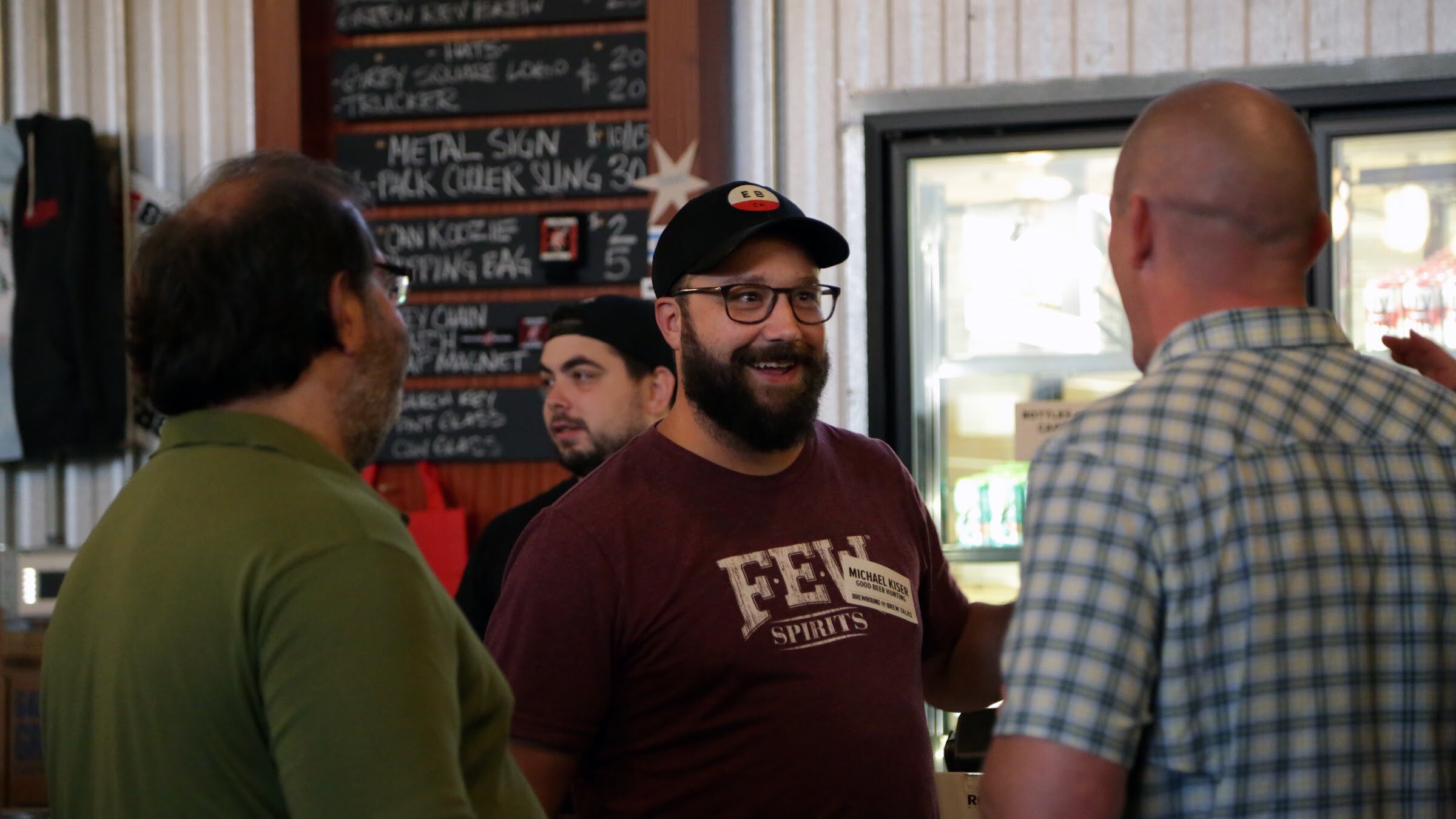 A bearded man in glasses and a maroon FEW Spirits shirt stands between two other guests.