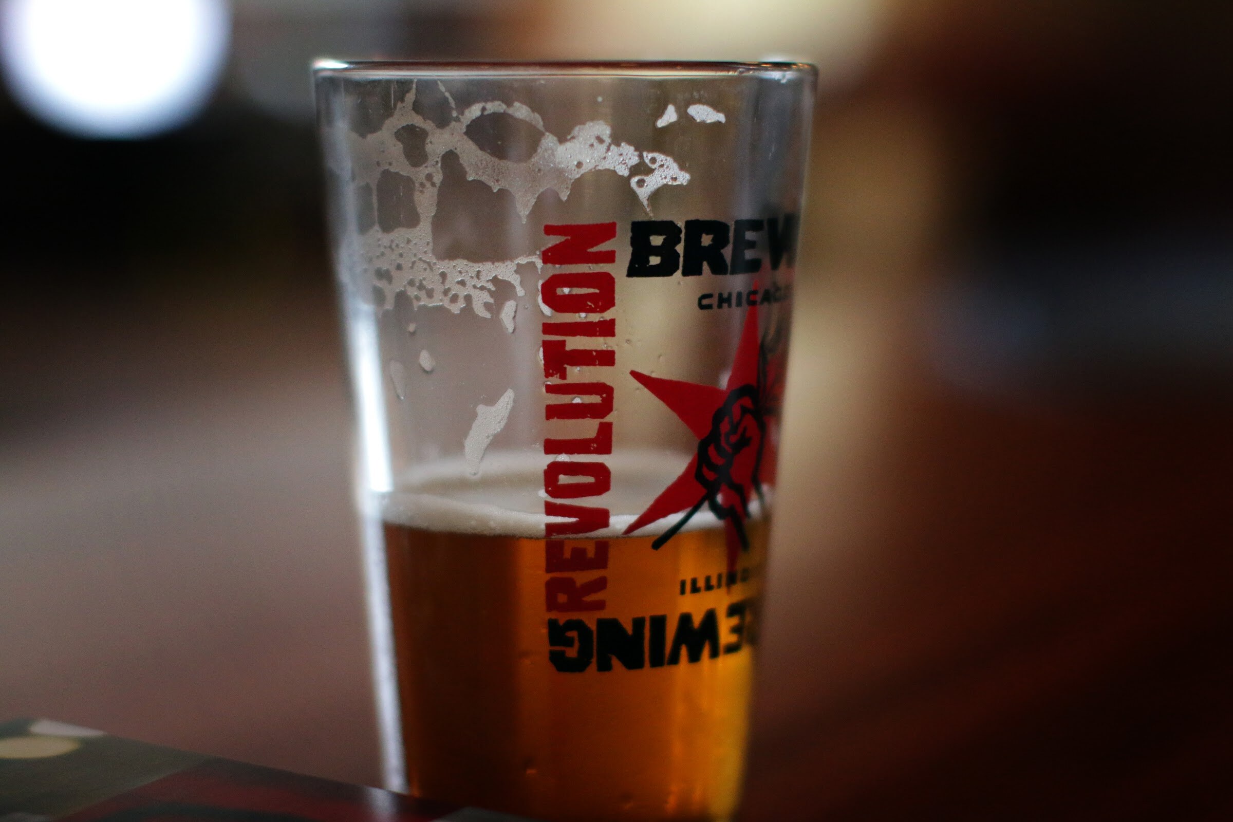 A close view shows golden beer and foam in a glass printed with Revolution Brewing lettering.