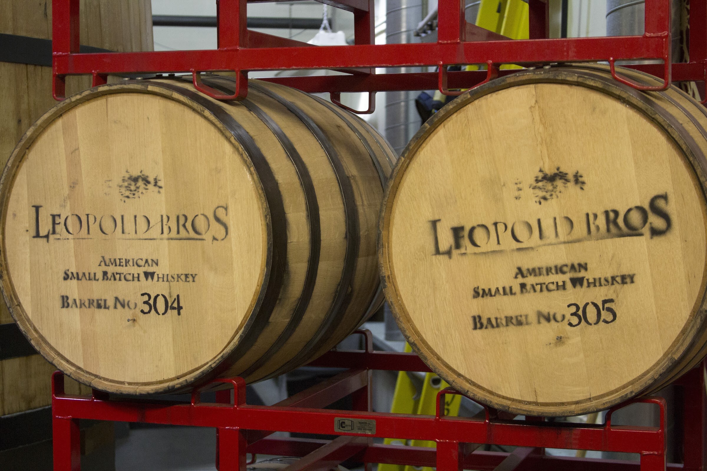 Two barrels marked Leopold Bros American Small Batch Whiskey rest side by side in a red metal rack.