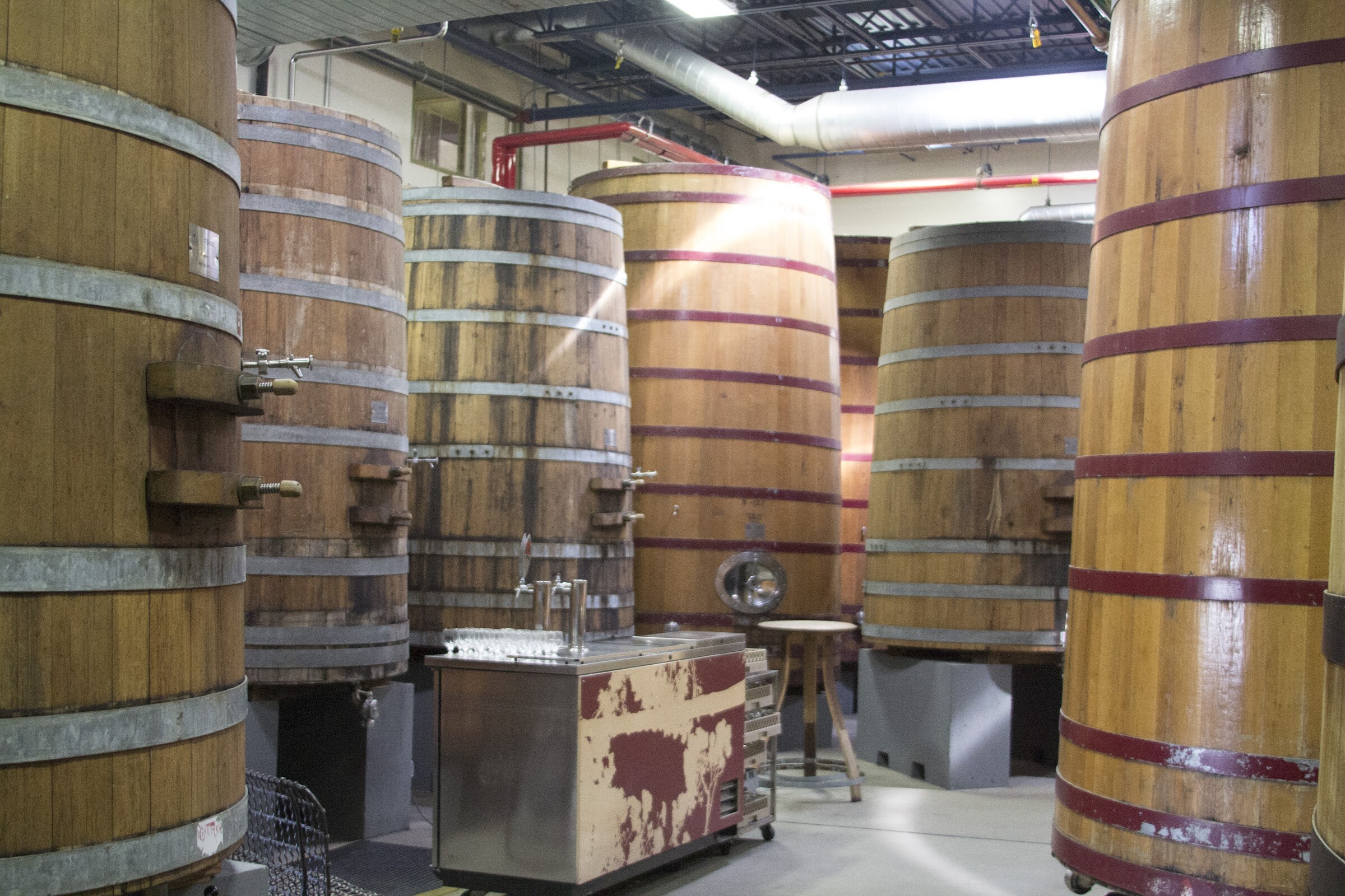 Large upright wooden vessels surround a small bar with taps and rows of glasses.