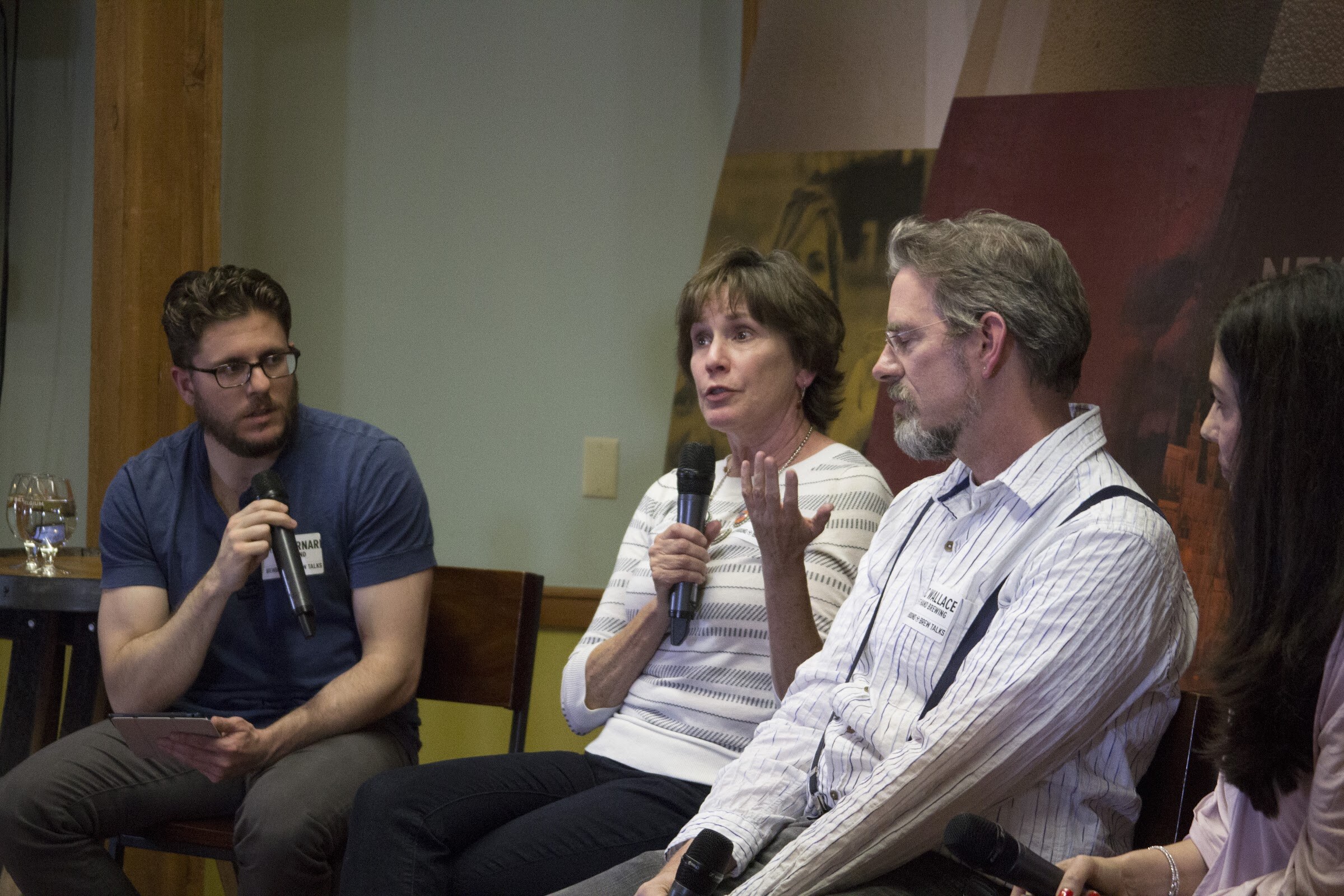 A woman in a white striped top speaks into a microphone between a moderator and two fellow panelists.