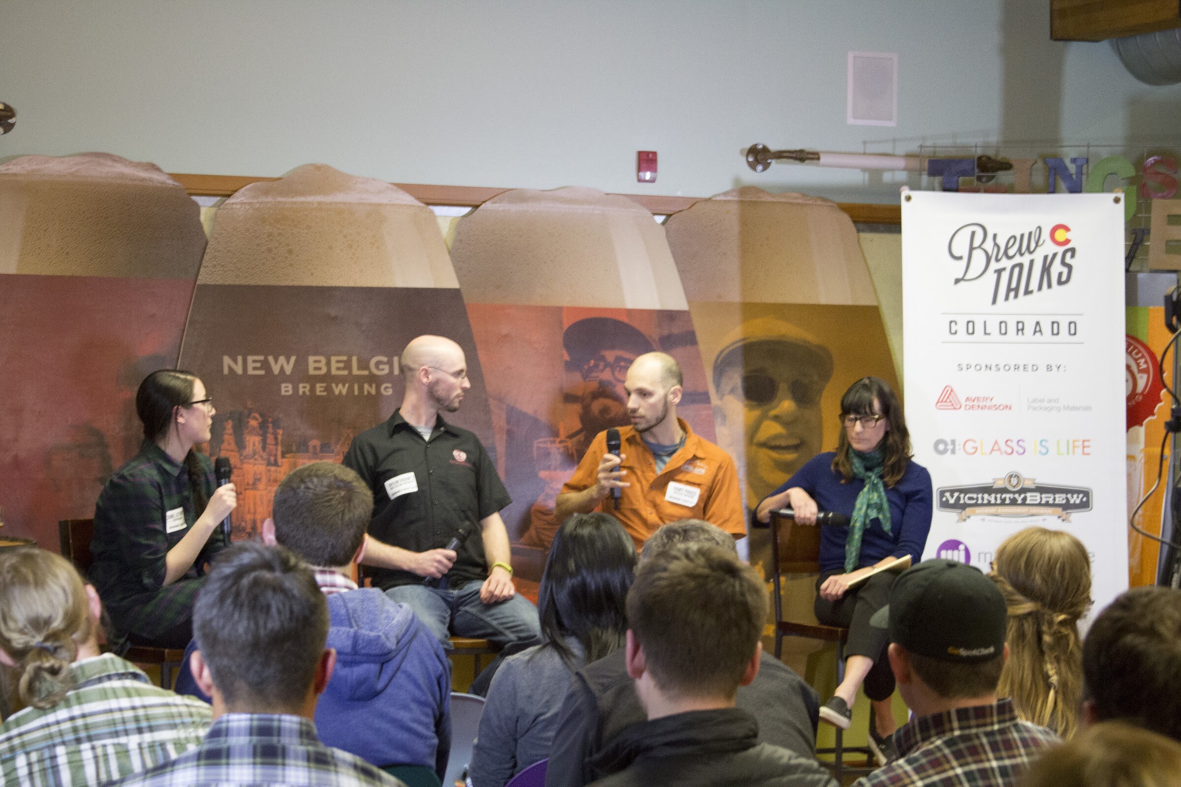Audience members face four seated speakers, with a Brew Talks Colorado banner at the right.