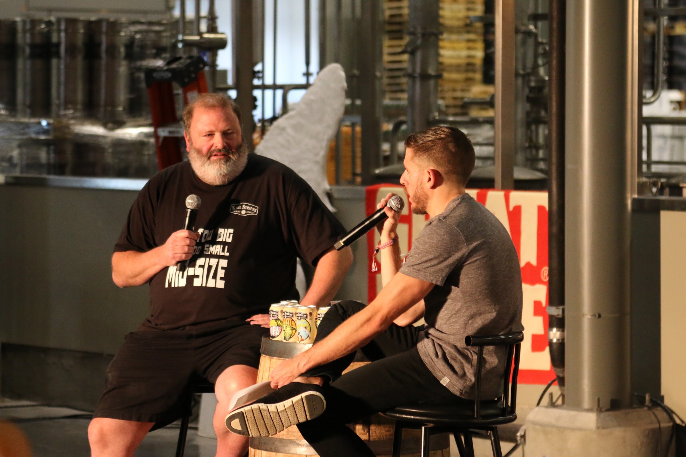 A bearded man with a microphone and the moderator sit close on stage with a row of beer cans on a barrel and a Great Divide sign behind them.
