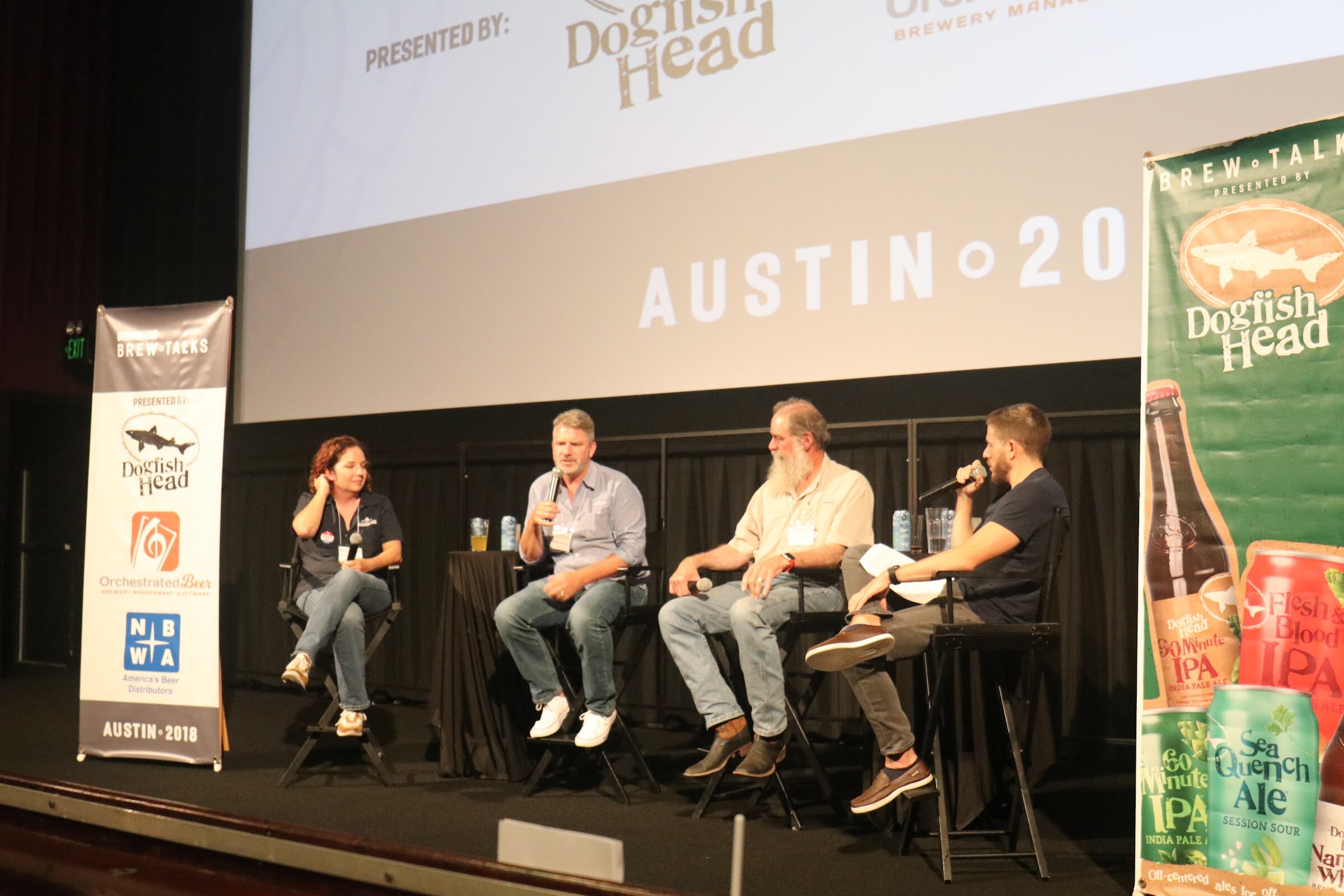 Four people seated on a stage in front of a screen partly showing Presented By Dogfish Head and Austin 2018, with a Dogfish Head beer banner at right.