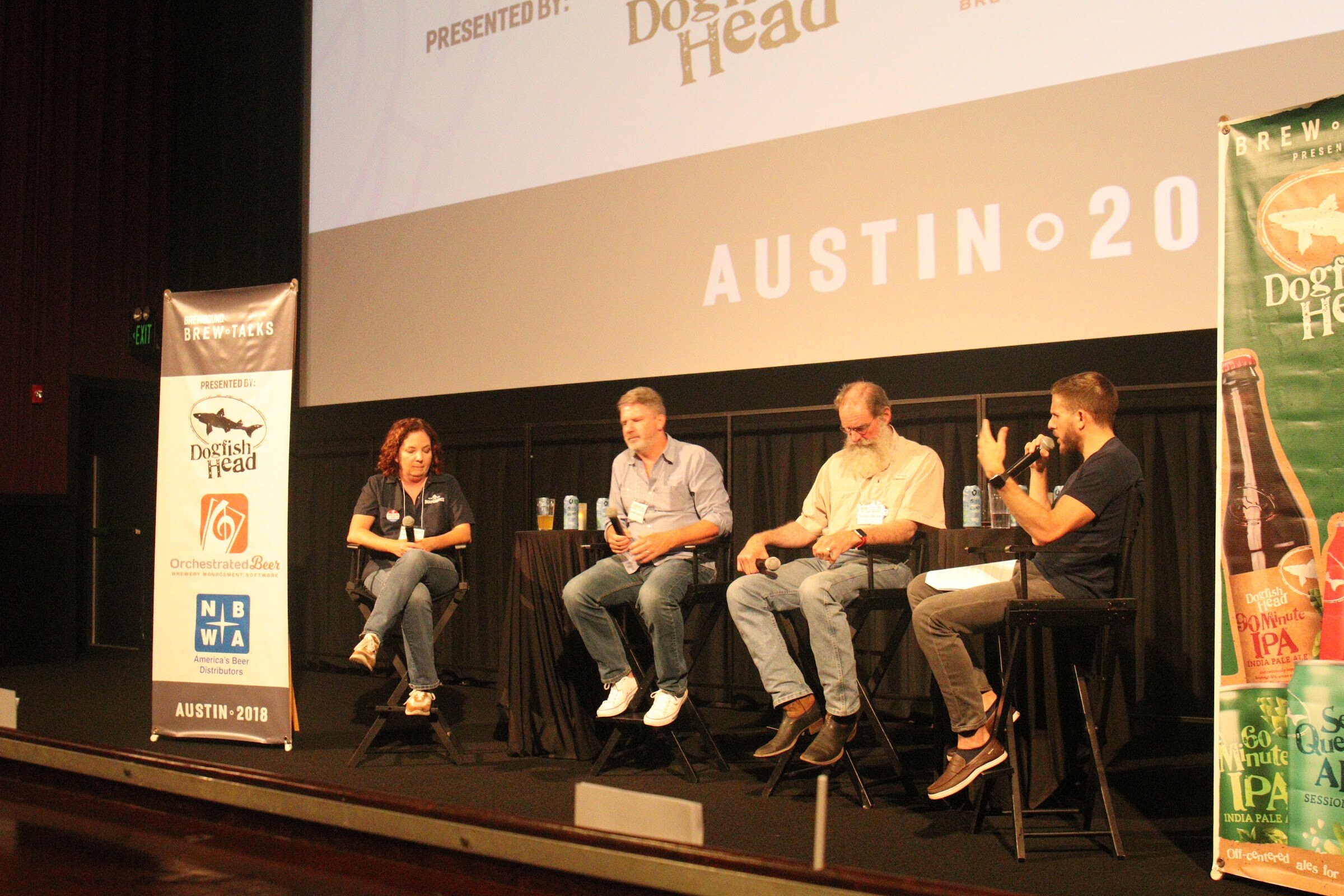 Three seated panelists and a moderator with a microphone on a stage beside banners for Dogfish Head, Orchestrated Beer and NBWA, under a screen reading Austin 2018.