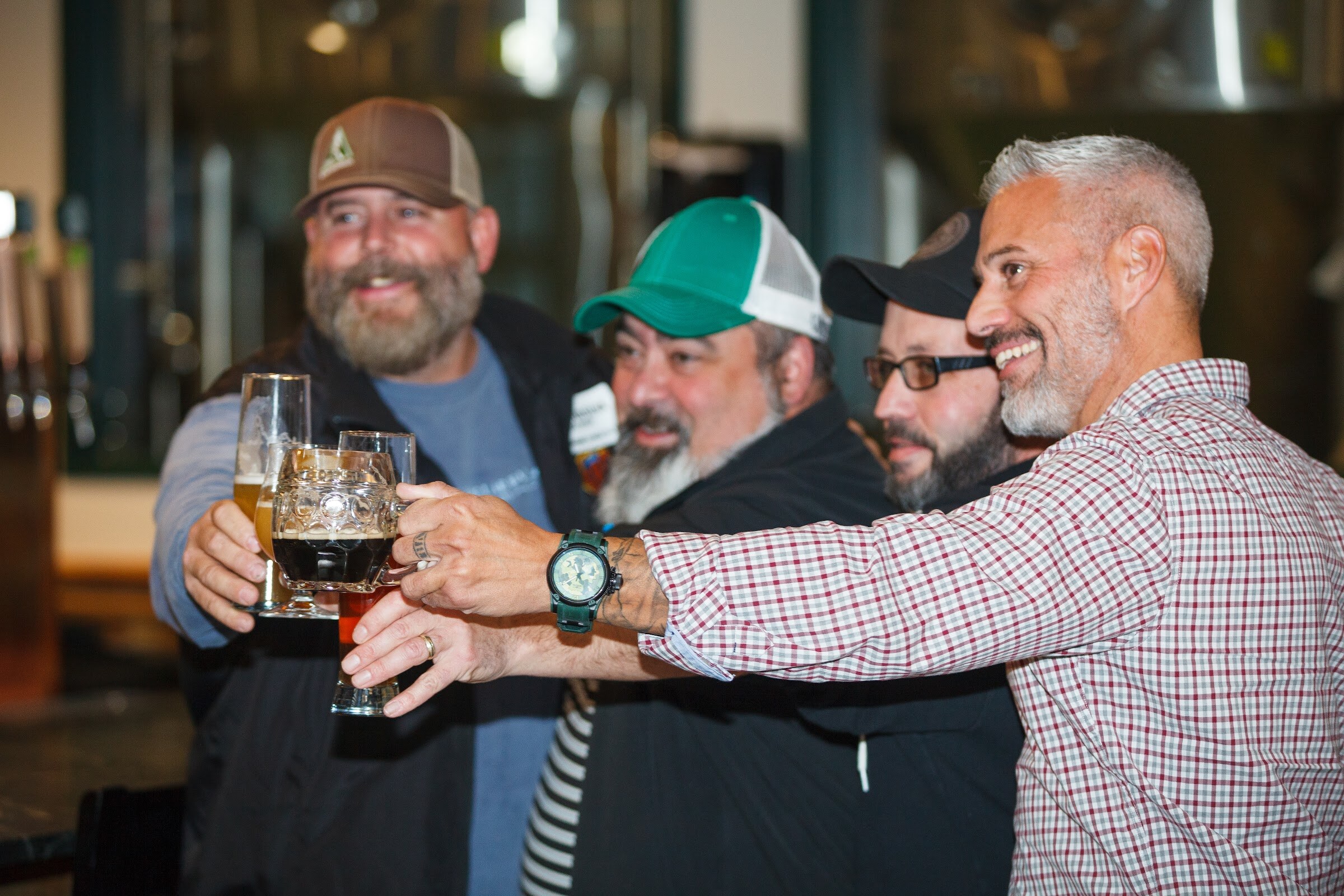 Four men lean together with raised glasses and mugs of beer.