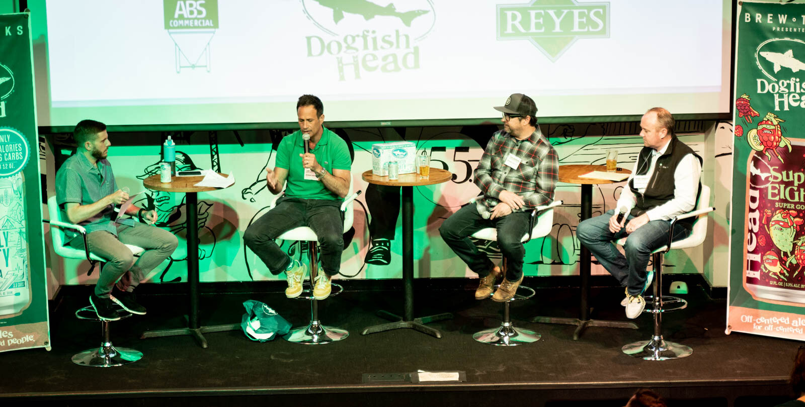 Four people seated on stools on a small stage beneath a screen showing Dogfish Head, Reyes and ABS Commercial logos.