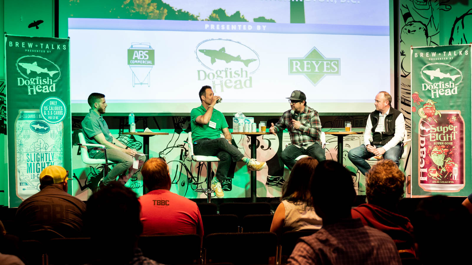 Wide view of four people on stage in a green-lit room with audience heads in the foreground.