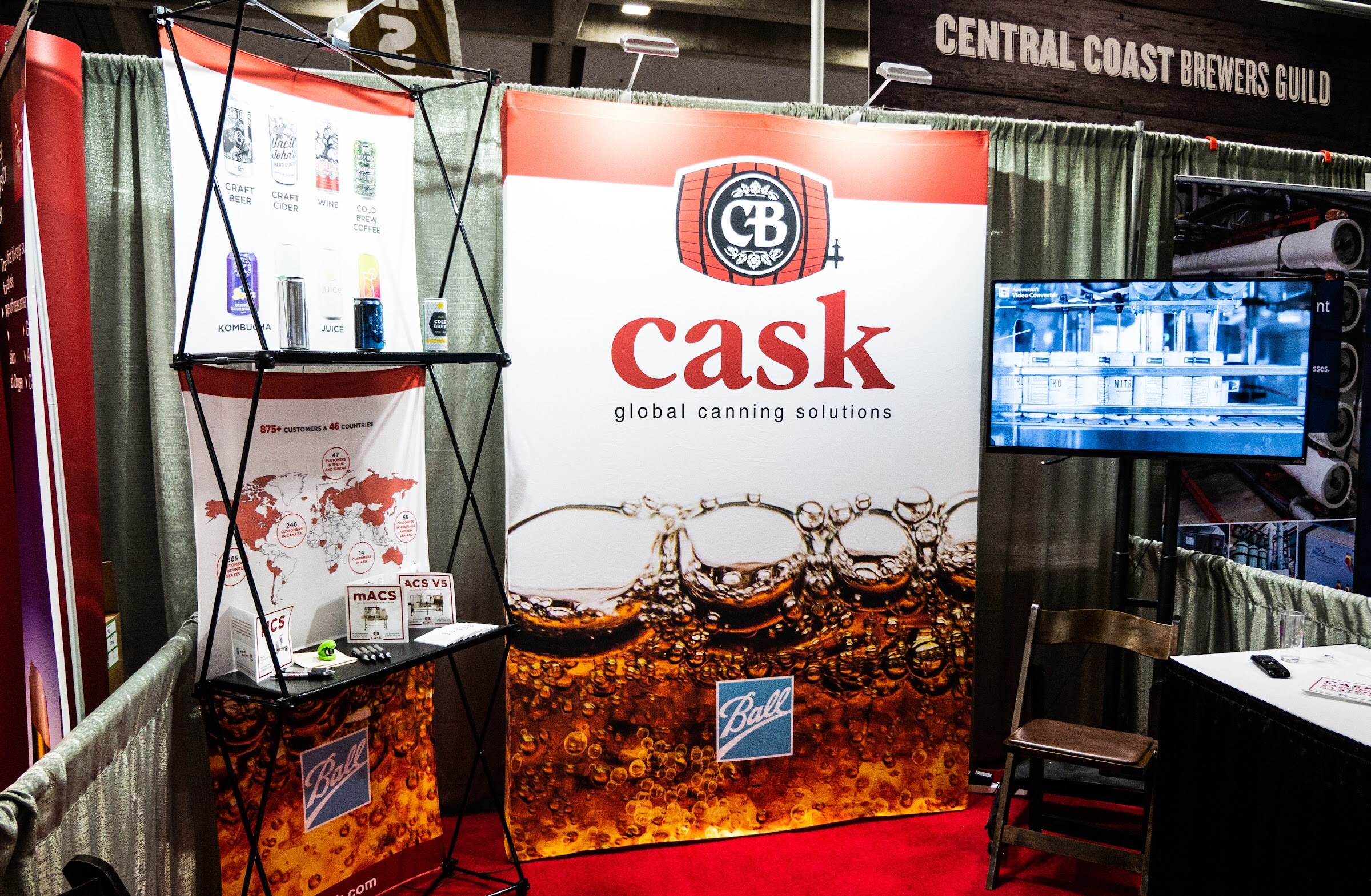 A trade show booth with a Cask global canning solutions banner with a Ball logo, a rack of can samples, a monitor and a Central Coast Brewers Guild sign above it.